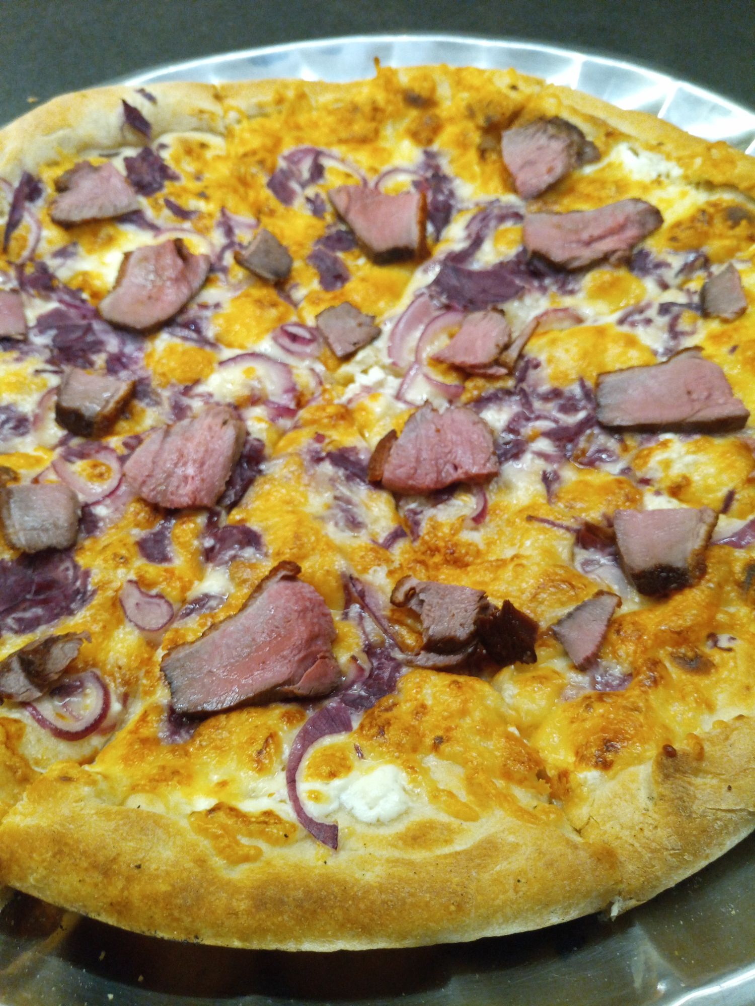 Pizza s mäsom, červenou cibuľou a syrovou polevou na chrumkavej kôrke.