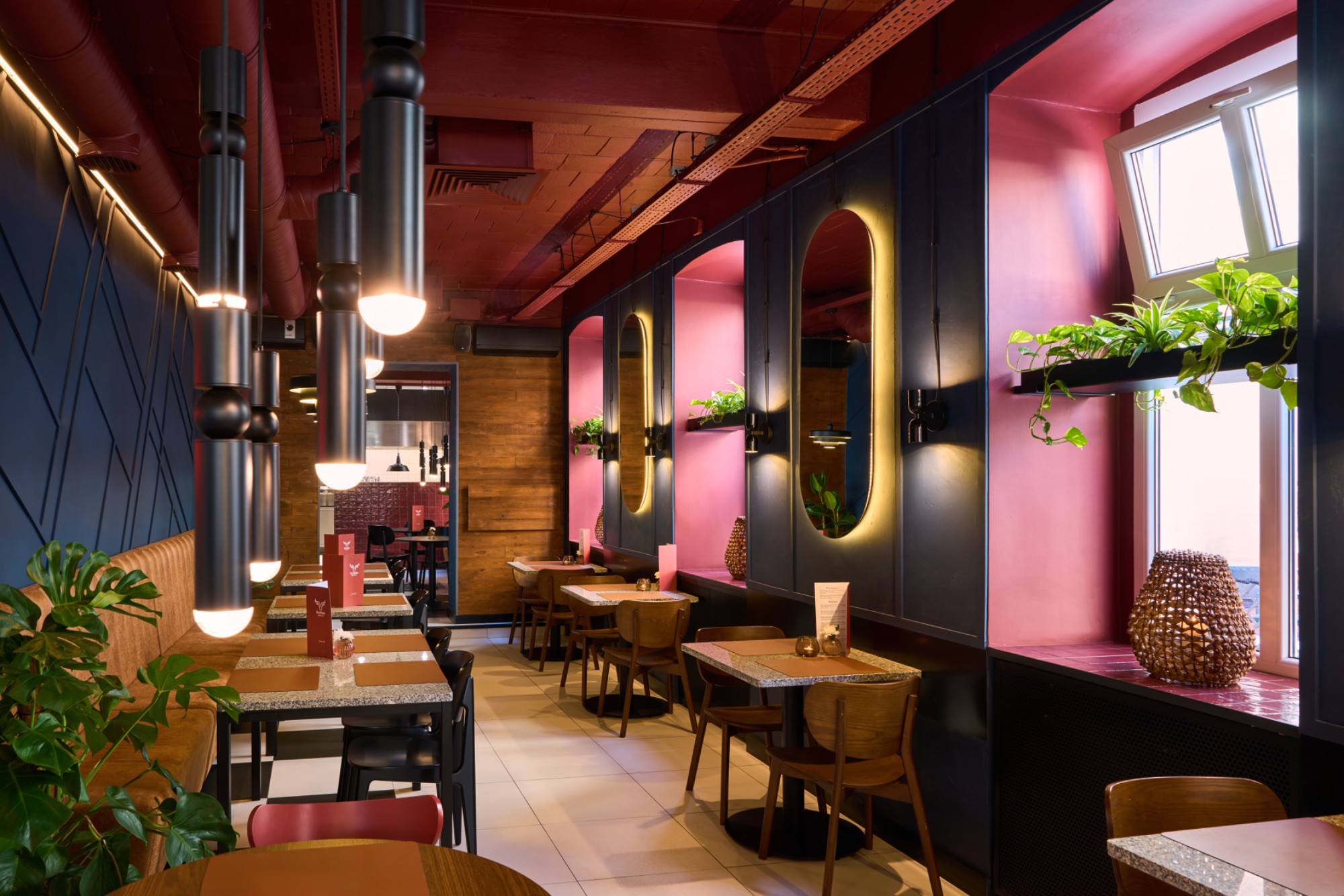 Nowoczesna restauracja z drewnianymi stołami, roślinami i klimatycznym oświetleniem.