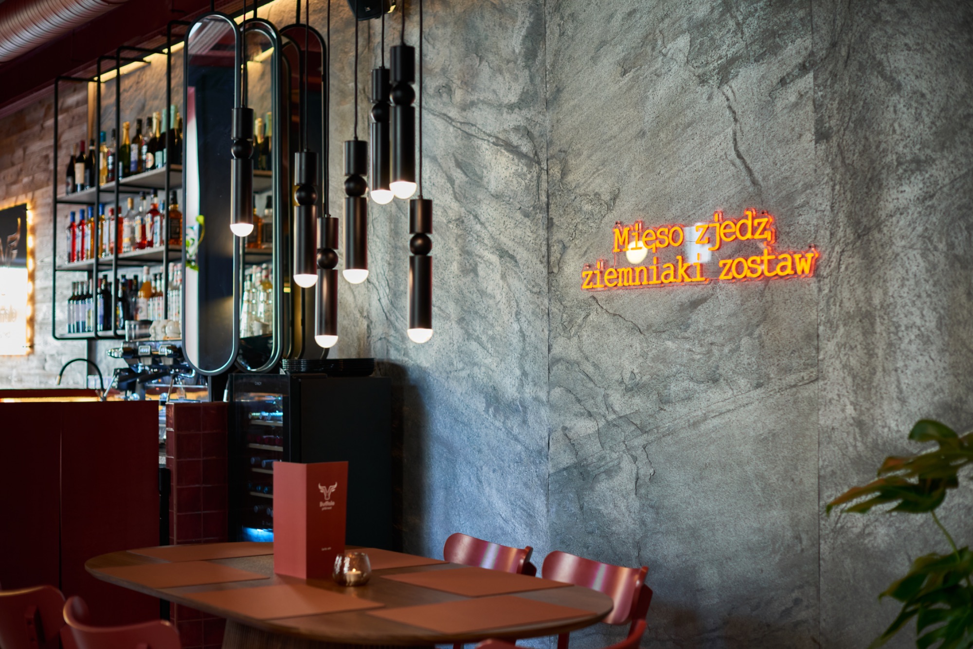 Nowoczesna restauracja z neonowym napisem i stylowym oświetleniem nad stołem.