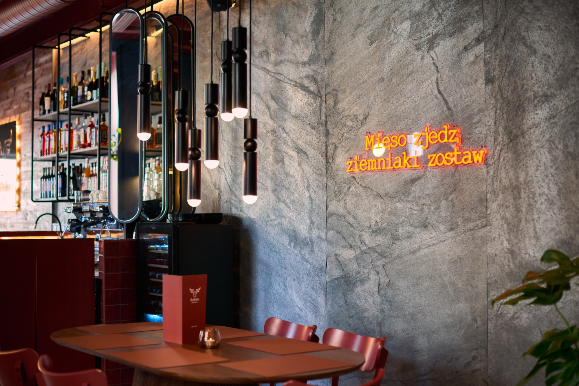 Stylowe wnętrze restauracji z oświetleniem, bar, neon z napisem "Mięso zjedz, ziemniaki zostaw".