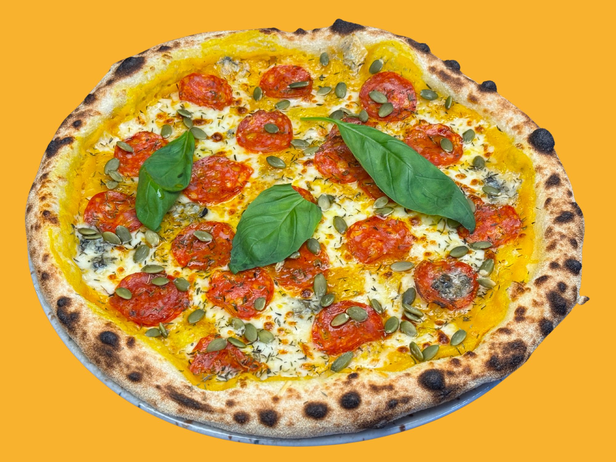Pizza z pepperoni, pestkami dyni i świeżą bazylią na złotym tle.