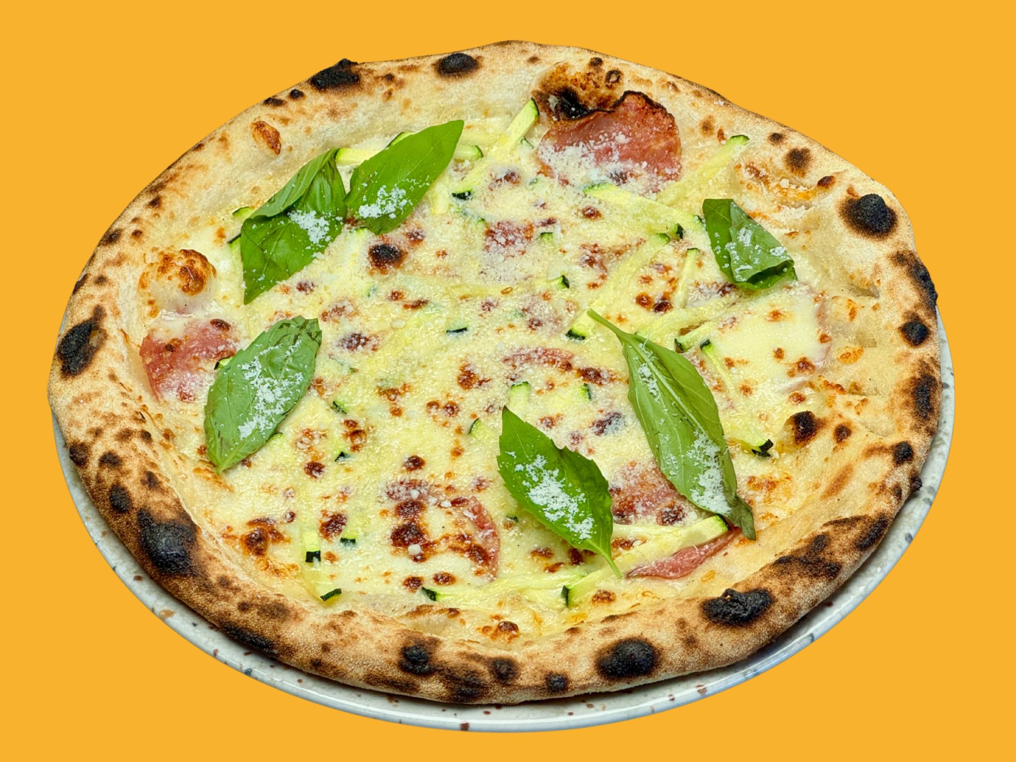 Pizza on a yellow background, topped with cheese, slices of salami, and fresh basil leaves.
