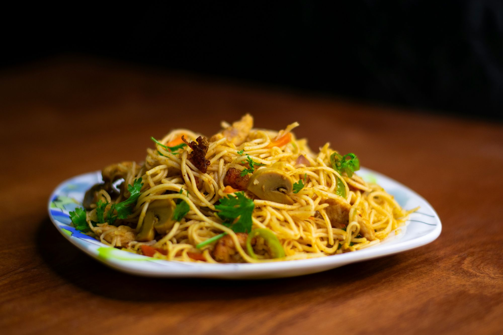 Talerz z makaronem stir-fry, udekorowanym ziołami, warzywami i kawałkami mięsa.