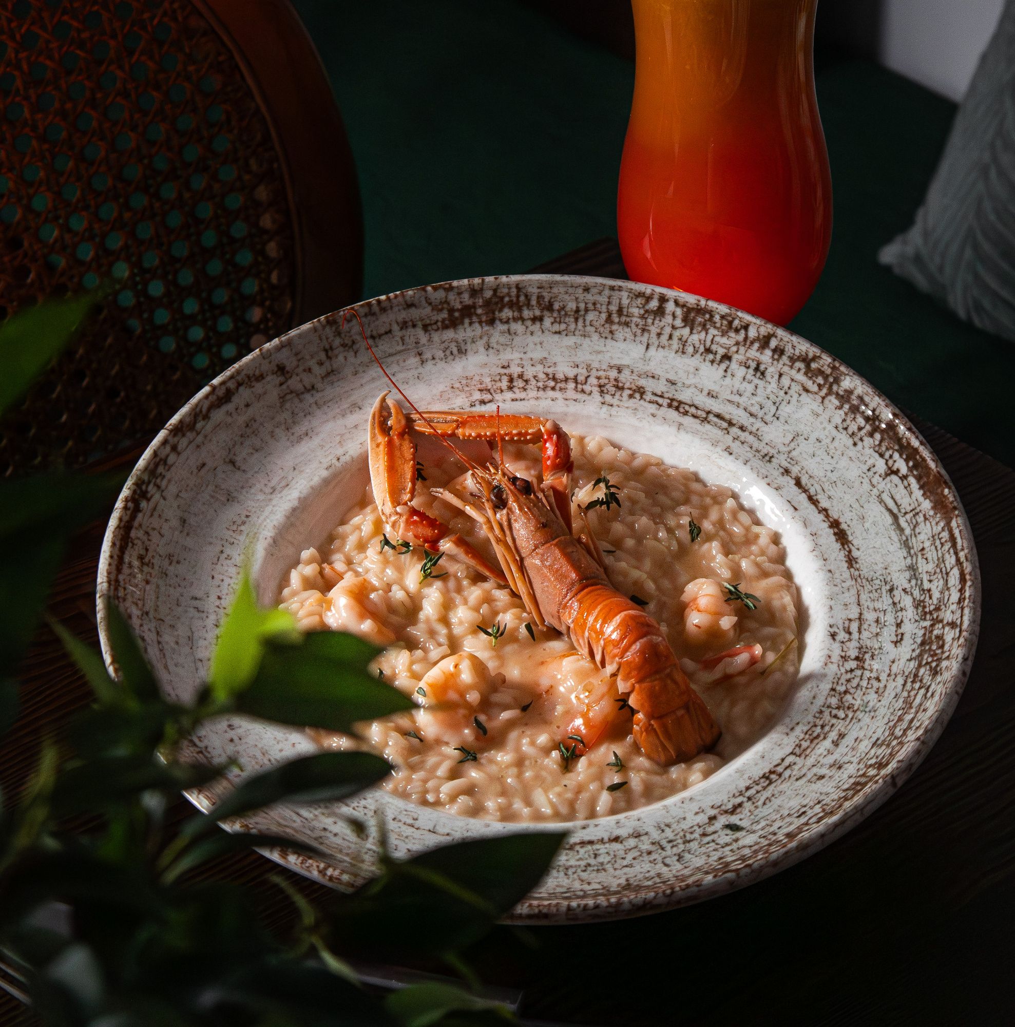Risotto z krewetkami i homarem, podane w głębokim talerzu, z kolorowym napojem w tle.
