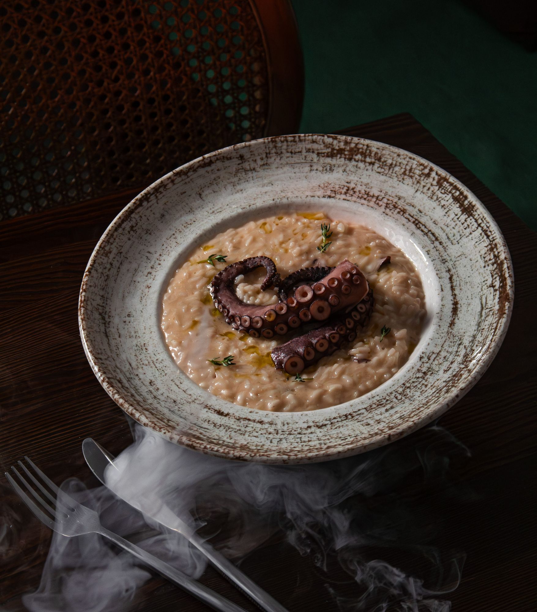 Risotto z ośmiornicą, podane w eleganckiej misce, z aromatycznymi ziołami i delikatną mgłą.