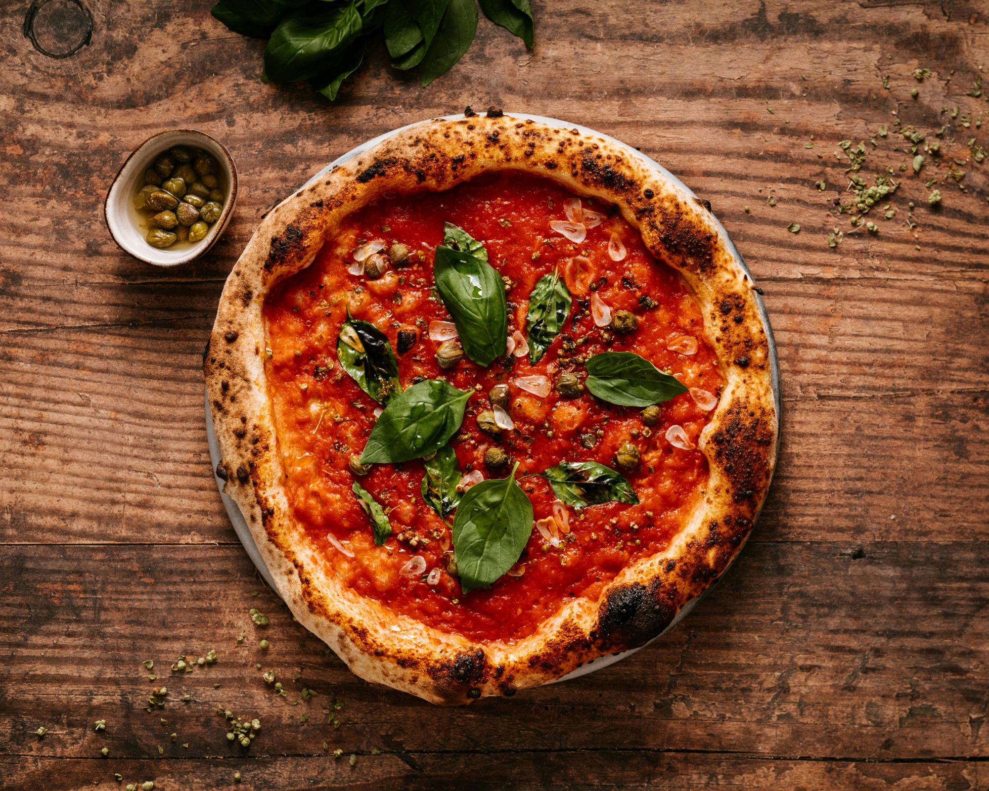 Pizza margherita z sosem pomidorowym, bazylią i oliwkami na drewnianym blacie.