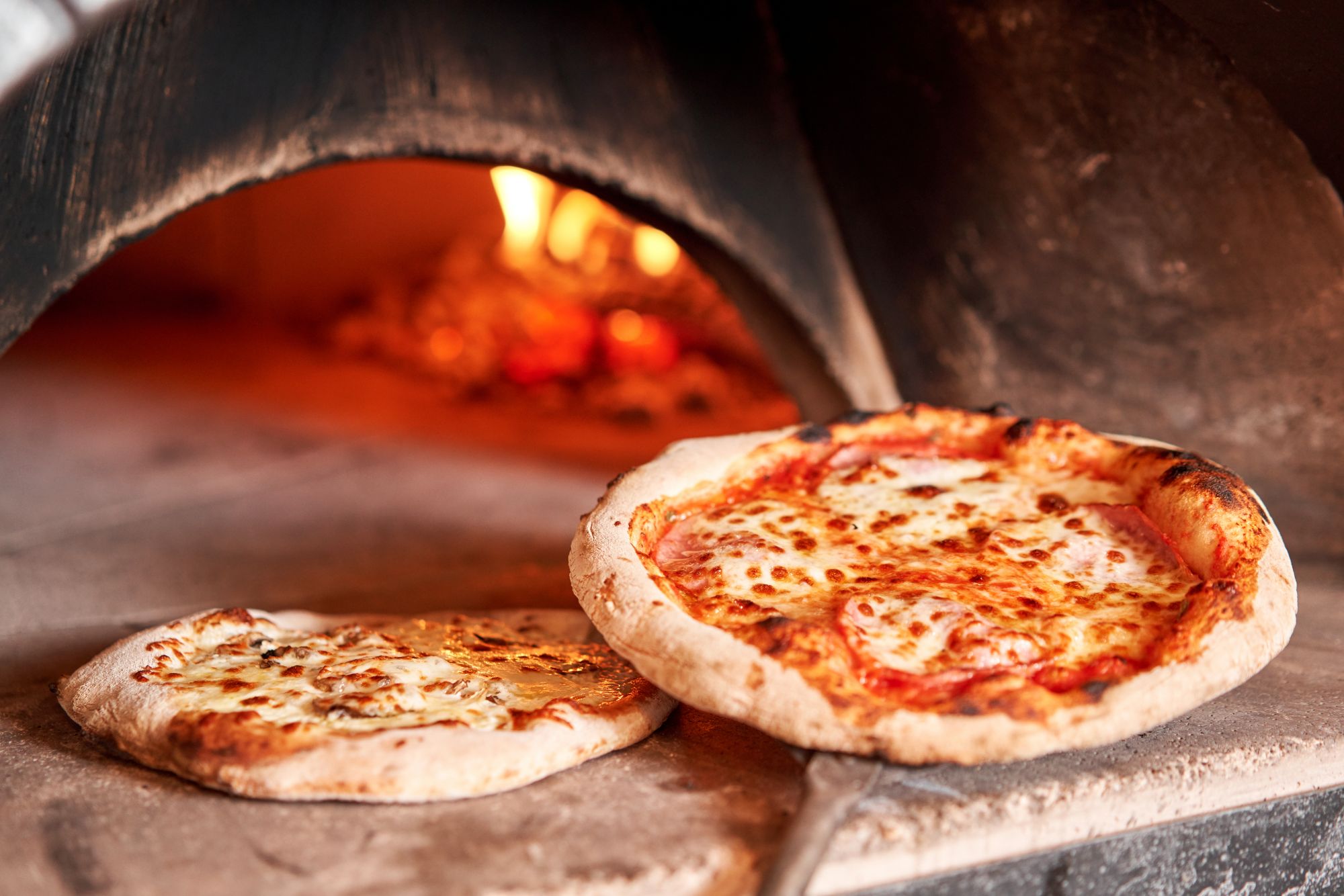Pizza wyjęta z pieca opalanego drewnem, z serem i sosem pomidorowym, na kamiennej powierzchni.