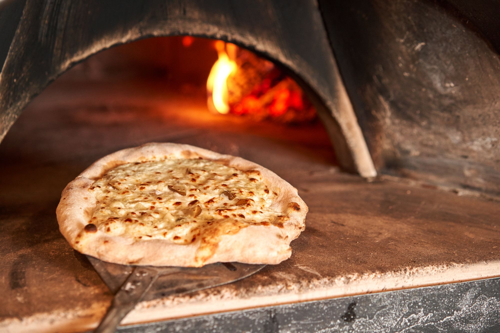 Pizze świeżo wyjęta z pieca opalanego drewnem, z chrupiącym ciastem i roztopionym serem.