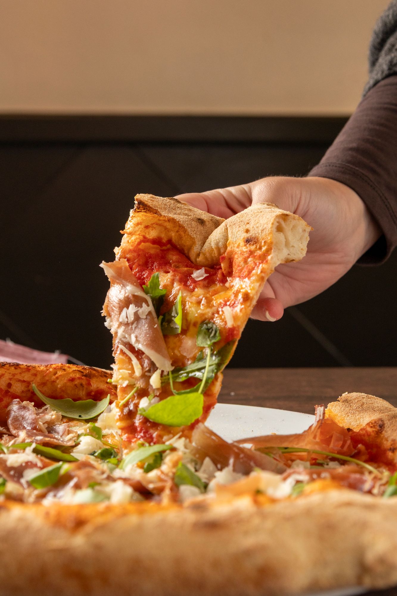Ręka sięga po kawałek pizzy z kawałkami kurczaka i świeżymi ziołami na talerzu.