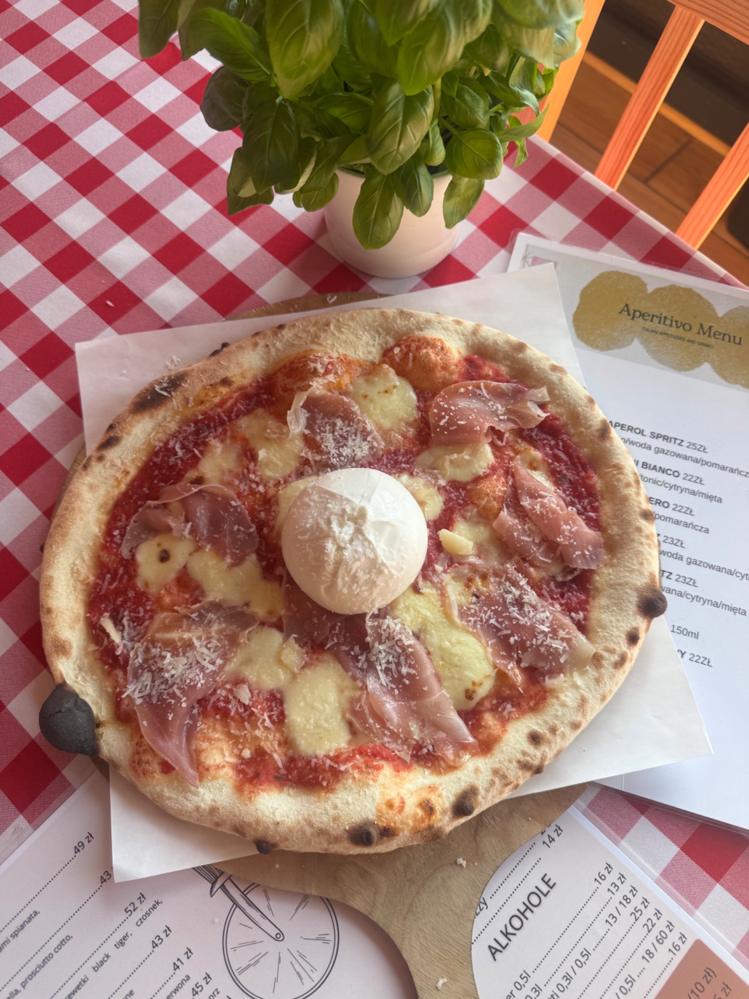 Pizza z sosem pomidorowym, serem mozzarella, szynką parmeńską, na stole w restauracji z bazylią w doniczce.
