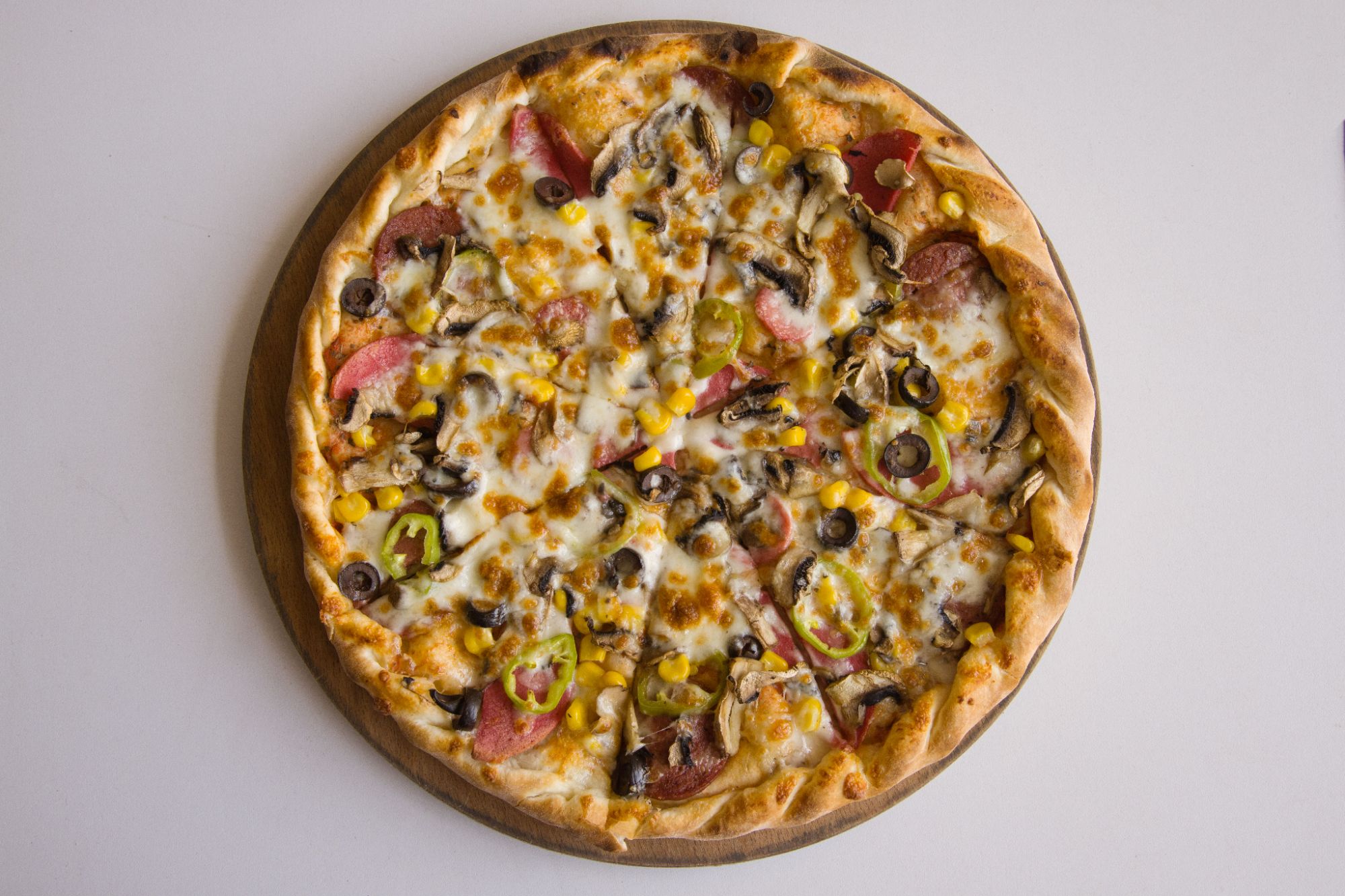 Pizza z serem, pepperoni, pieczarkami, oliwkami, papryczkami, kukurydzą na drewnianej desce.