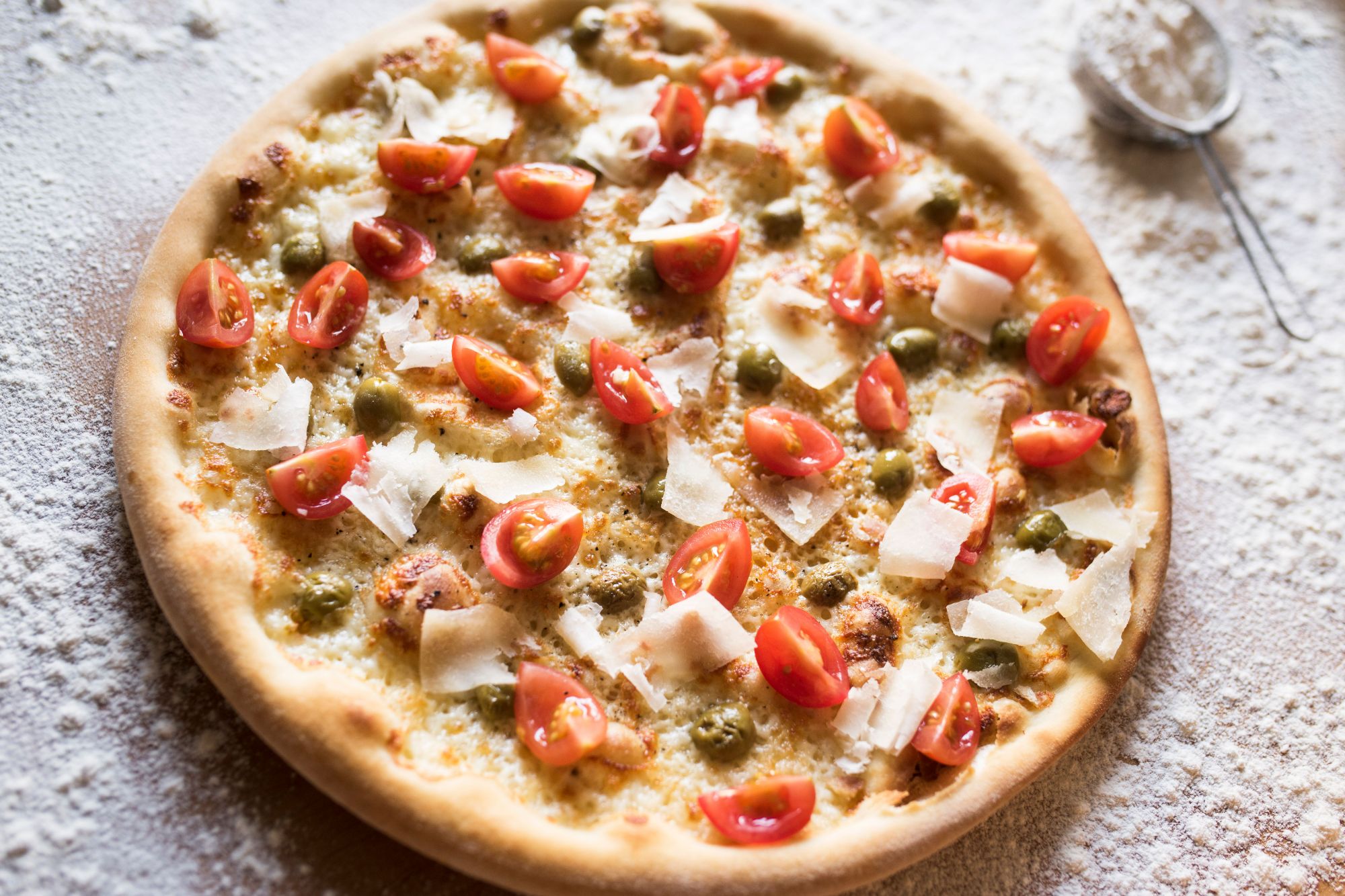 Pizza z pomidorkami koktajlowymi, serem parmezan i sosem pesto, posypana mąką.