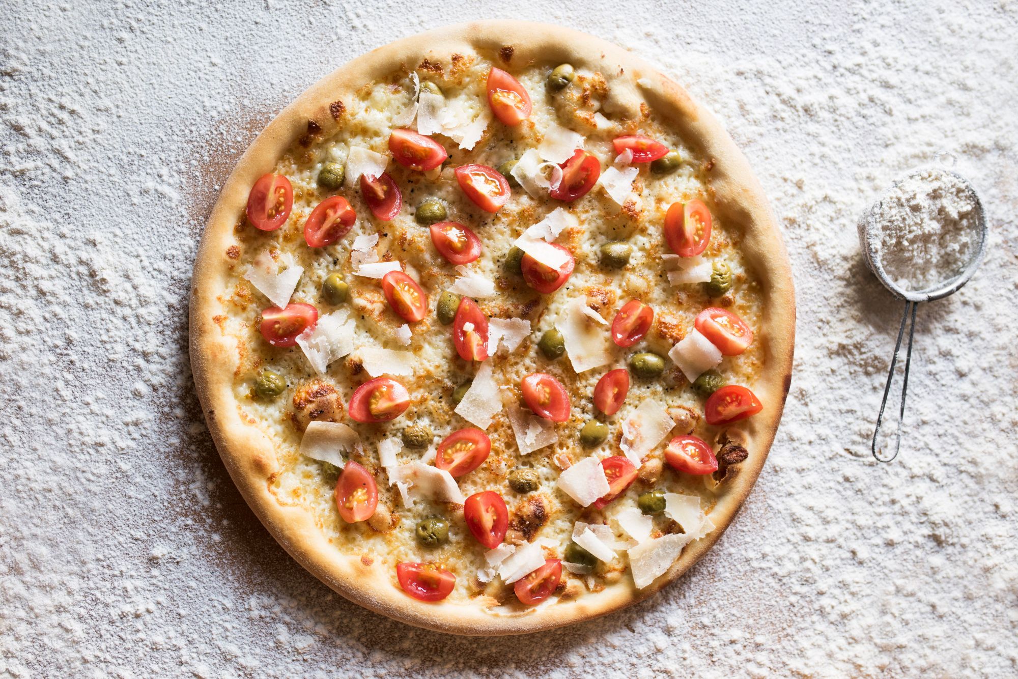 Pizza z pomidorkami, serem parmezan i sosem na tle mąki.