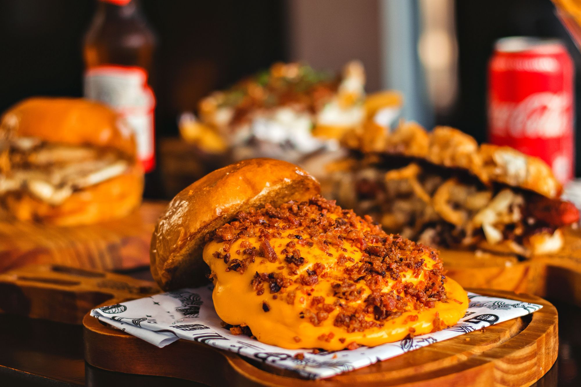 Soczysty burger z serem cheddar i boczkiem na tle innych potraw fast food, w klimatycznej restauracji.