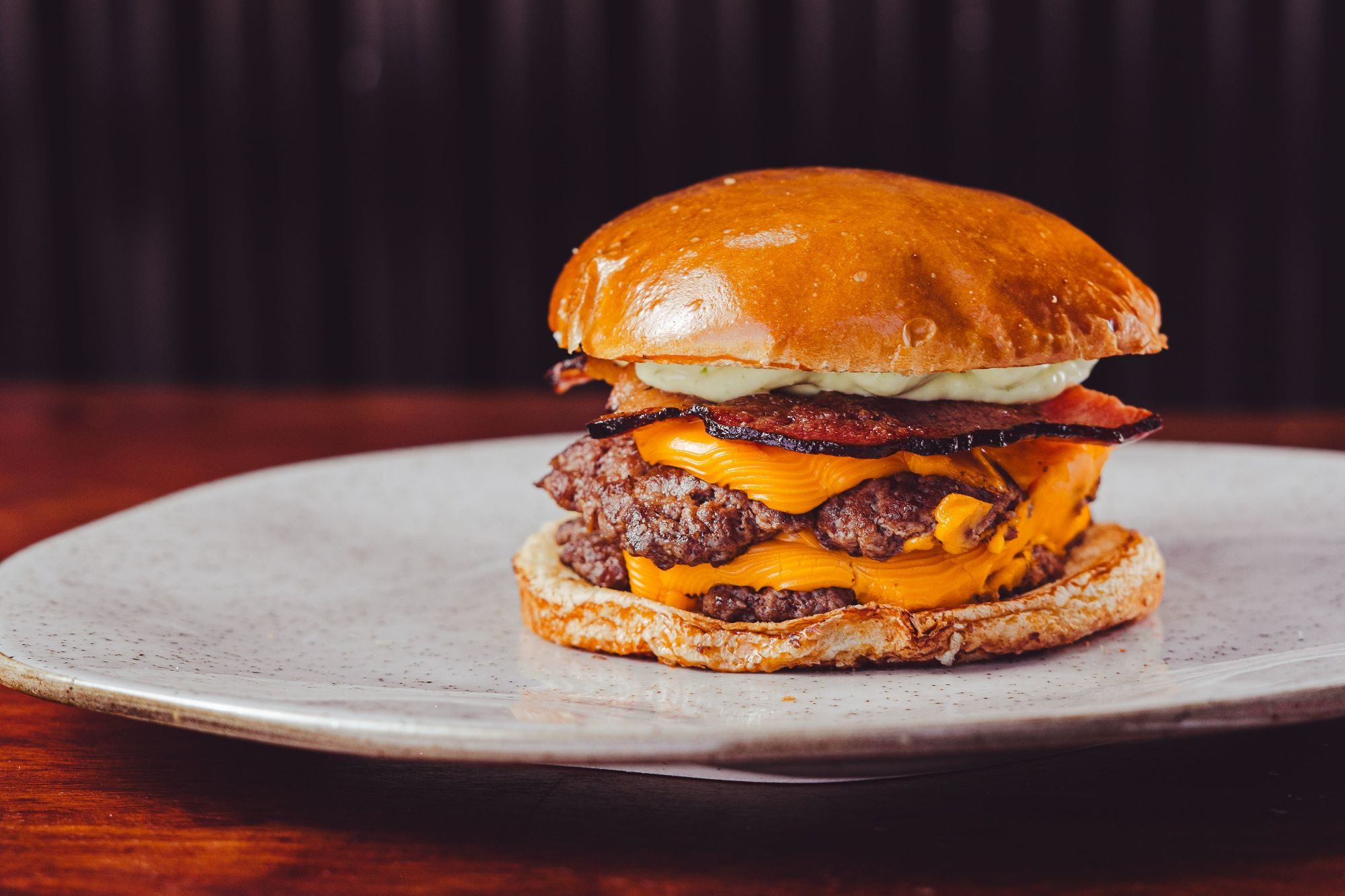 Soczysty burger z wołowiny, serem cheddar, bekonem i majonezem na bułce, podany na talerzu.