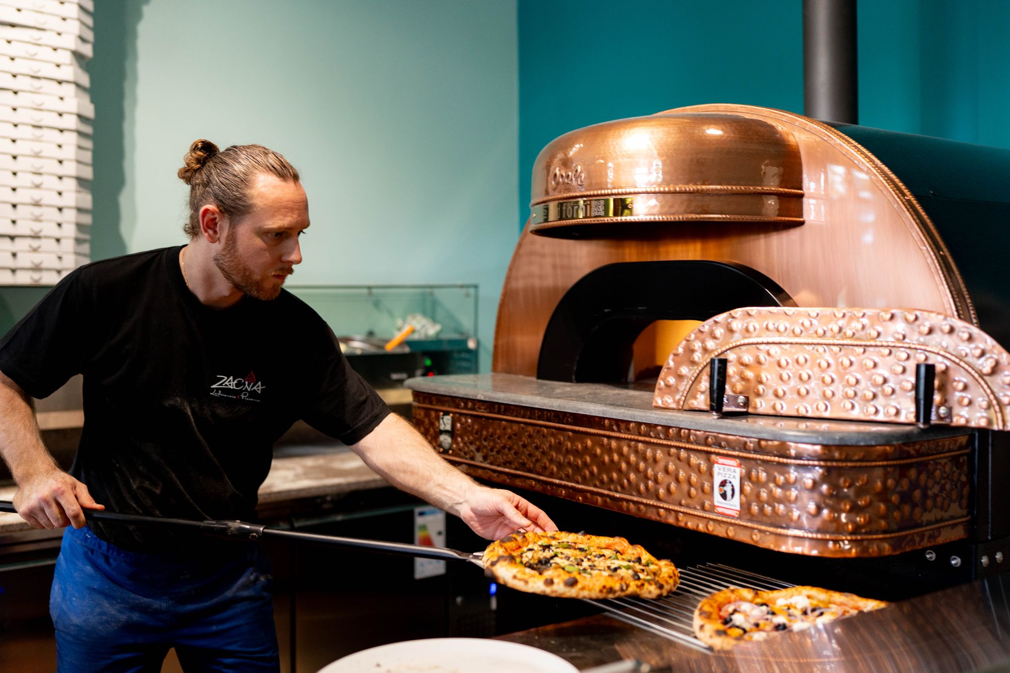 Mężczyzna wyciąga pizzę z profesjonalnego pieca do pizzy w restauracji.