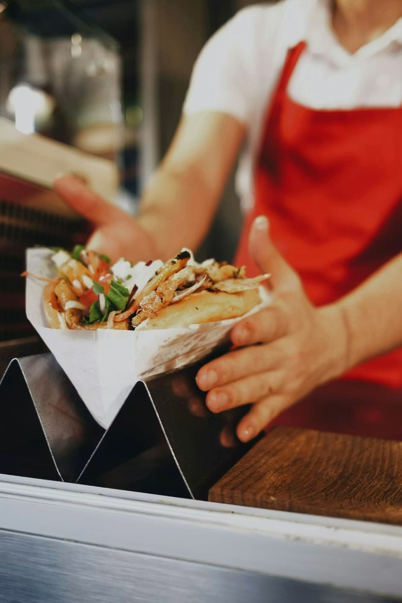 Kucharz podaje porcję frytek w papierowej misce, z sałatą i pomidorami, w restauracji z muralem w tle.