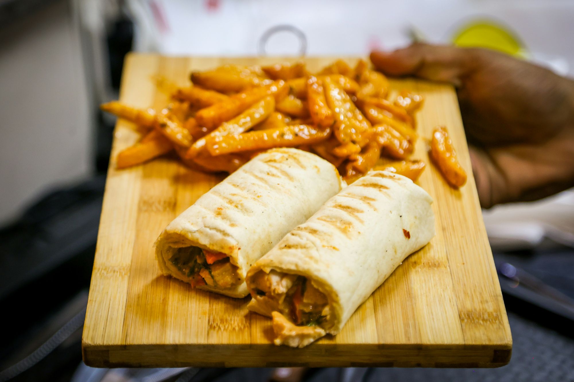 Talerz z dwoma burrito w tortilli i frytkami, podany na drewnianej desce.