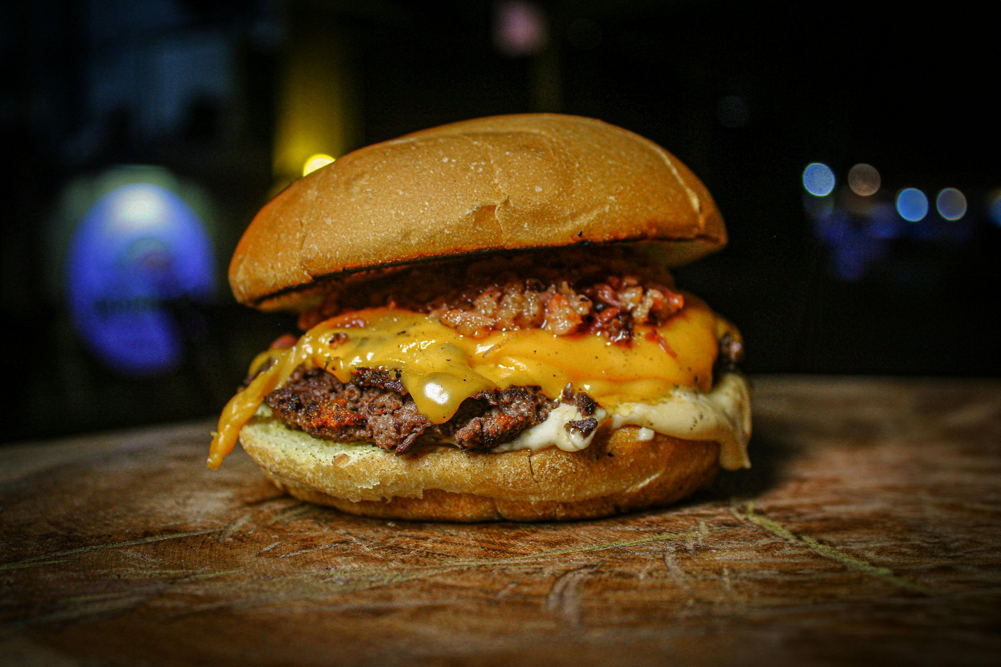 Soczysty burger z serem cheddar, chrupiącym bekonem i miękką bułką na tle rozmytego tła.