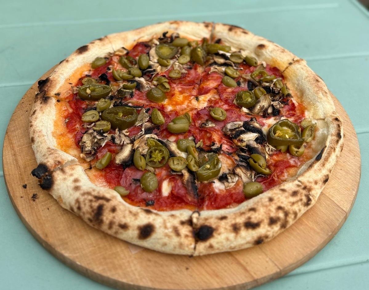 Pizza z sosem pomidorowym, pieczarkami i oliwkami, na drewnianej desce do krojenia.