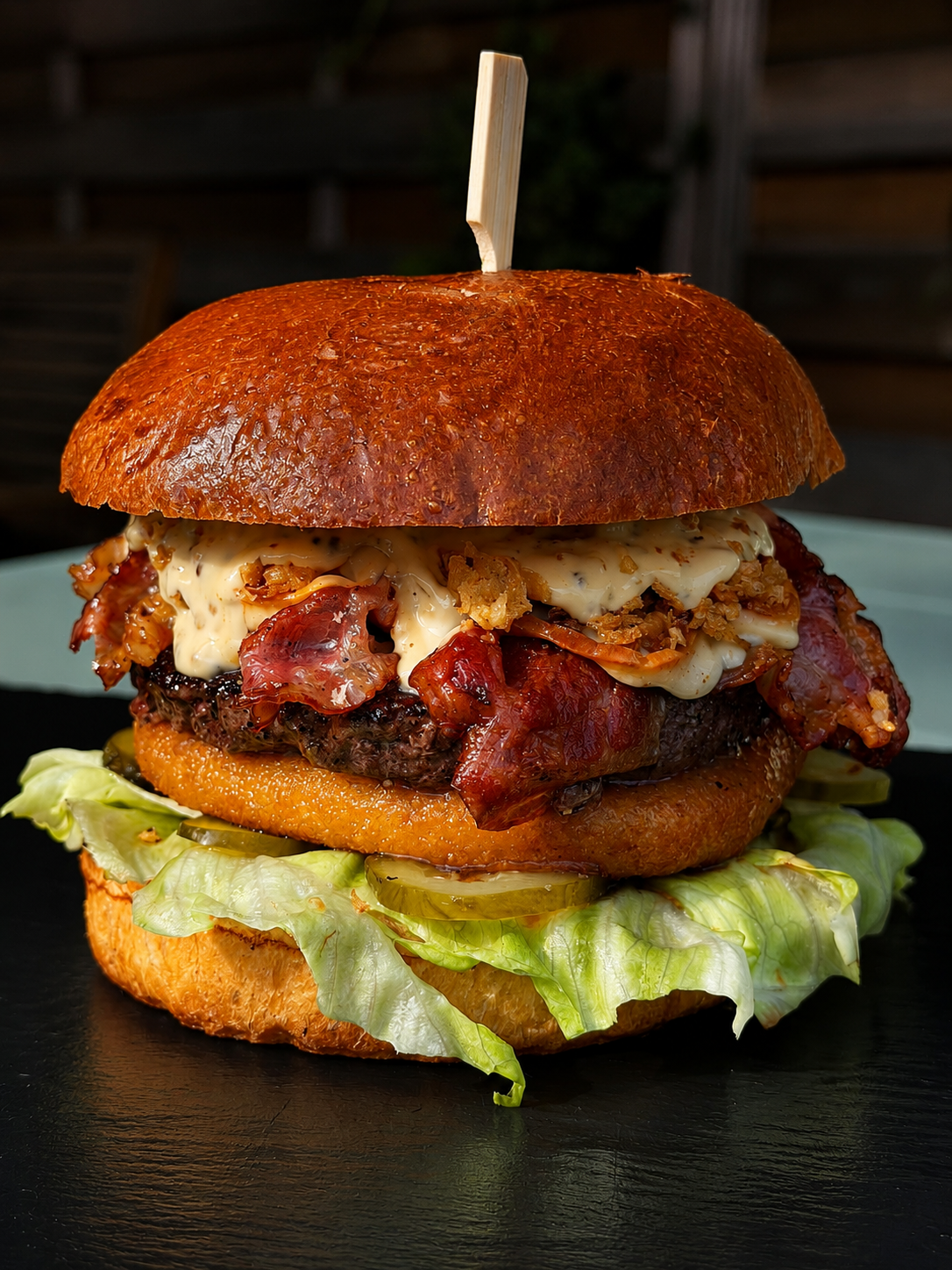 Soczysty hamburger z bekonem, smażoną cebulą i sosem na maślanej bułce, podany na sałacie.