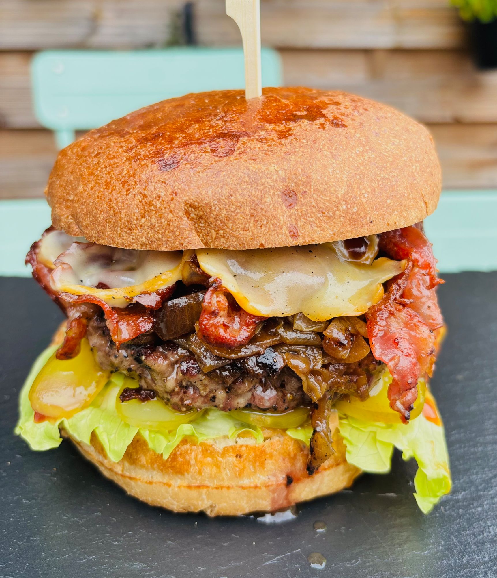 Soczysty burger z mięsem, serem, bekonem, cebulą, sałatą i bułką pszenną, podany na talerzu.