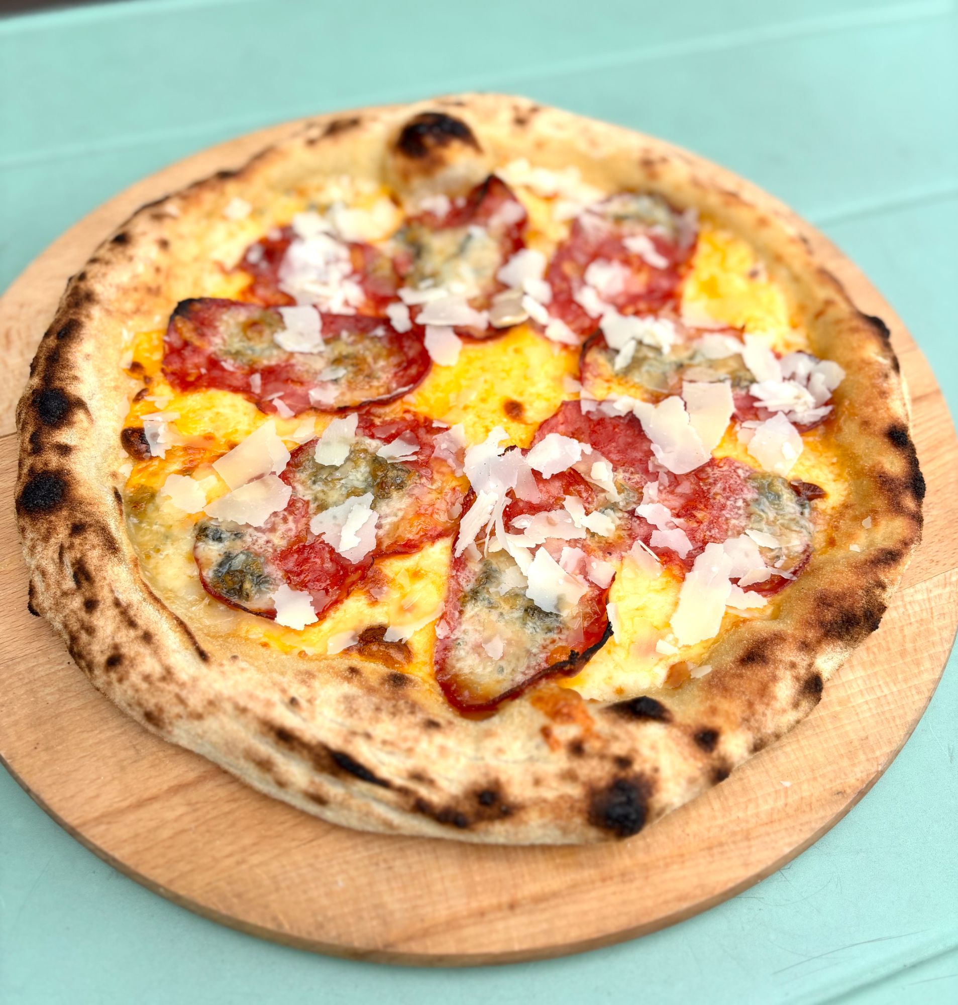 Pizza z serem i salami na drewnianej desce, z widocznymi chrupiącymi brzegami.