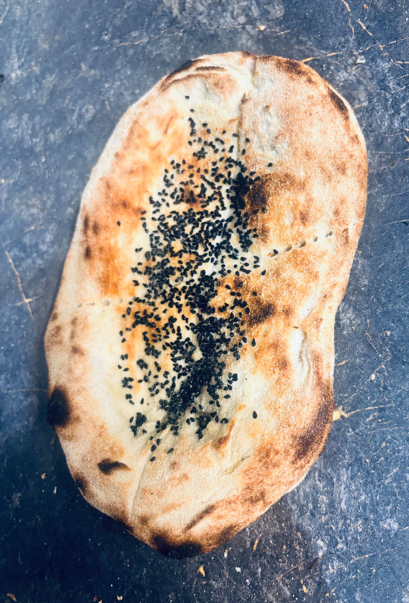 Chlebek naan z czarnuszką na szarej powierzchni, lekko przypieczony z brzegami.