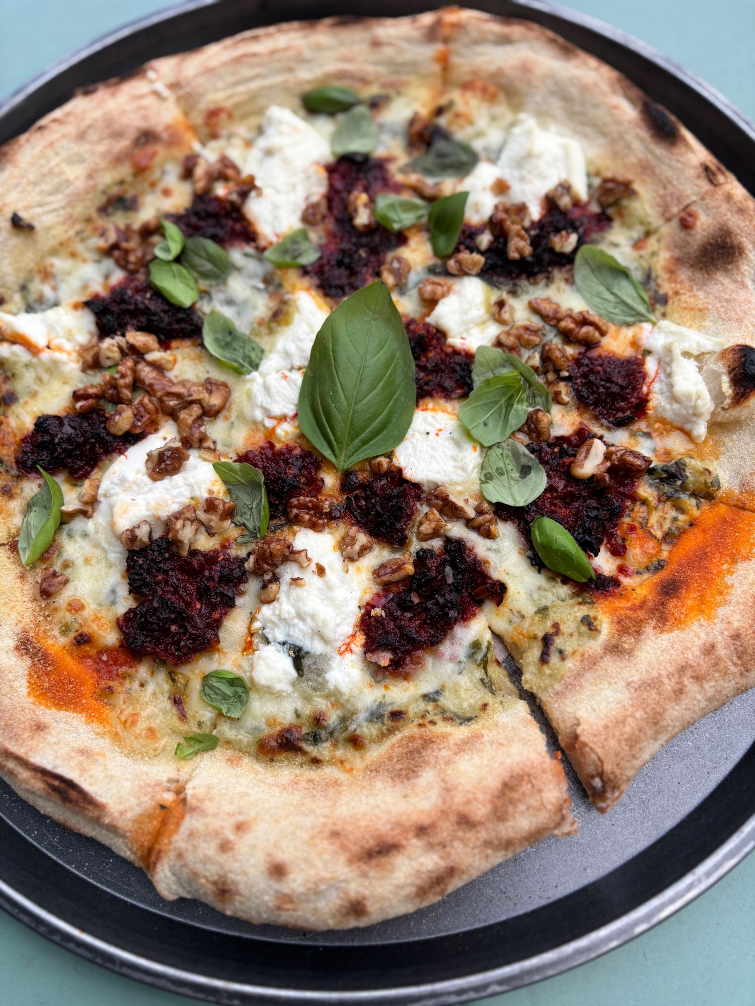 Pizza z serem ricotta, orzechami i bazylią, na chrupiącym cieście, podana na talerzu.