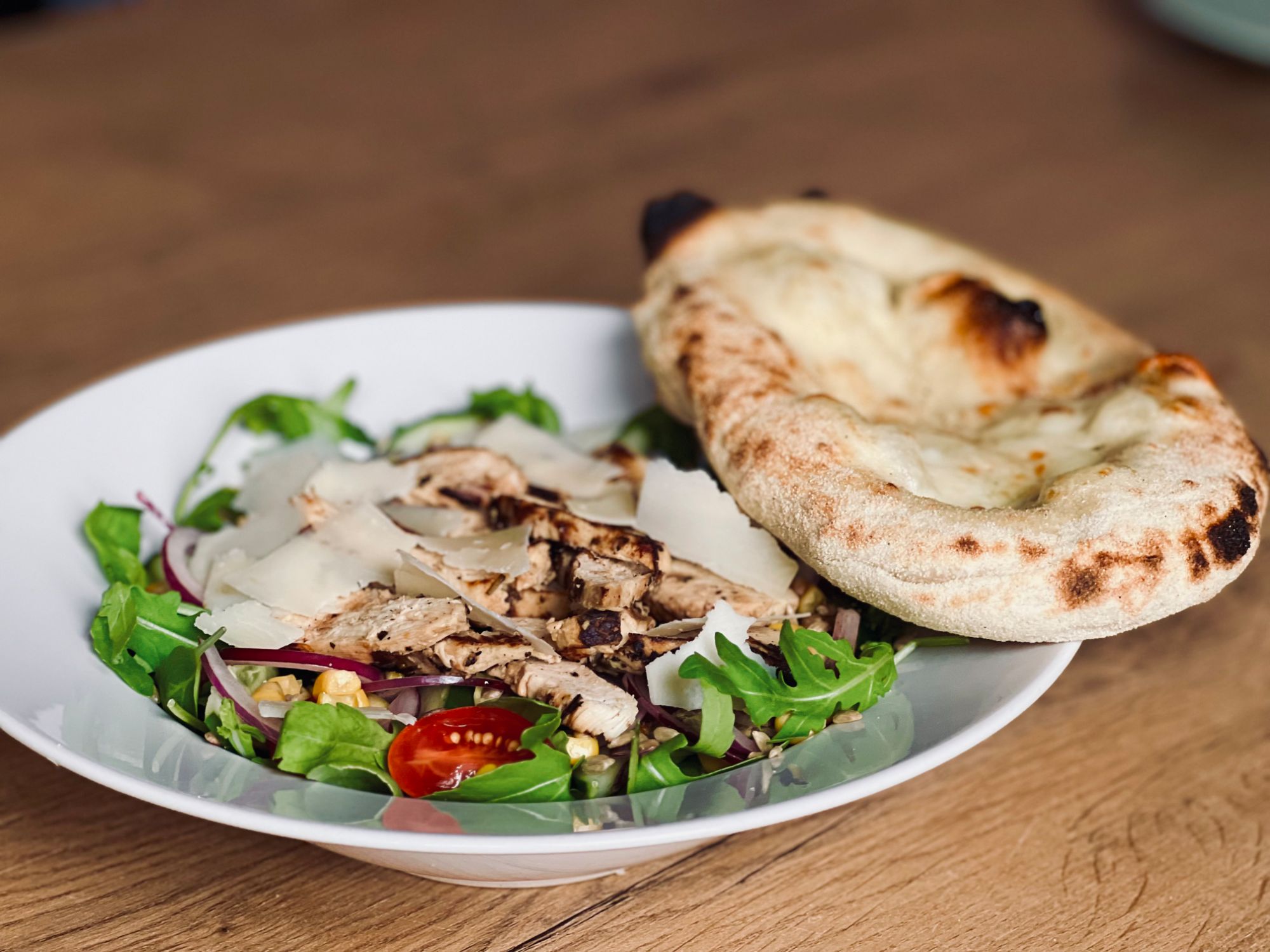 Sałatka z grillowanym kurczakiem, serem, pomidorem i chlebem pita na talerzu.