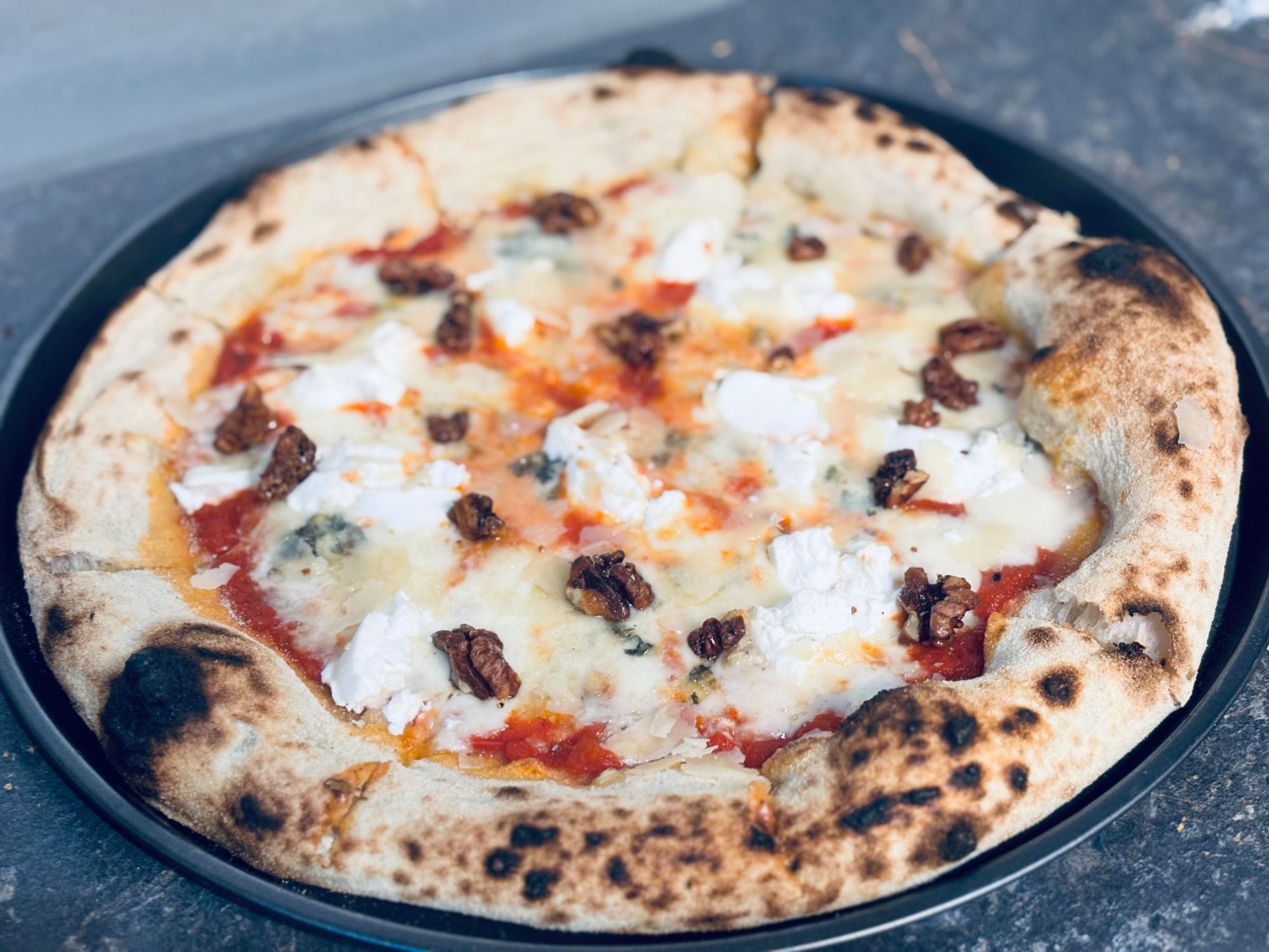 Pizza na czarnym talerzu z serem, sosem pomidorowym i orzechami.