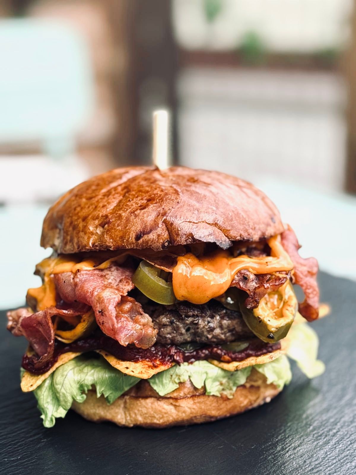 Soczysty burger z bekonem, serem, papryką jalapeño i sałatą w chrupiącej bułce, podany na czarnym talerzu.