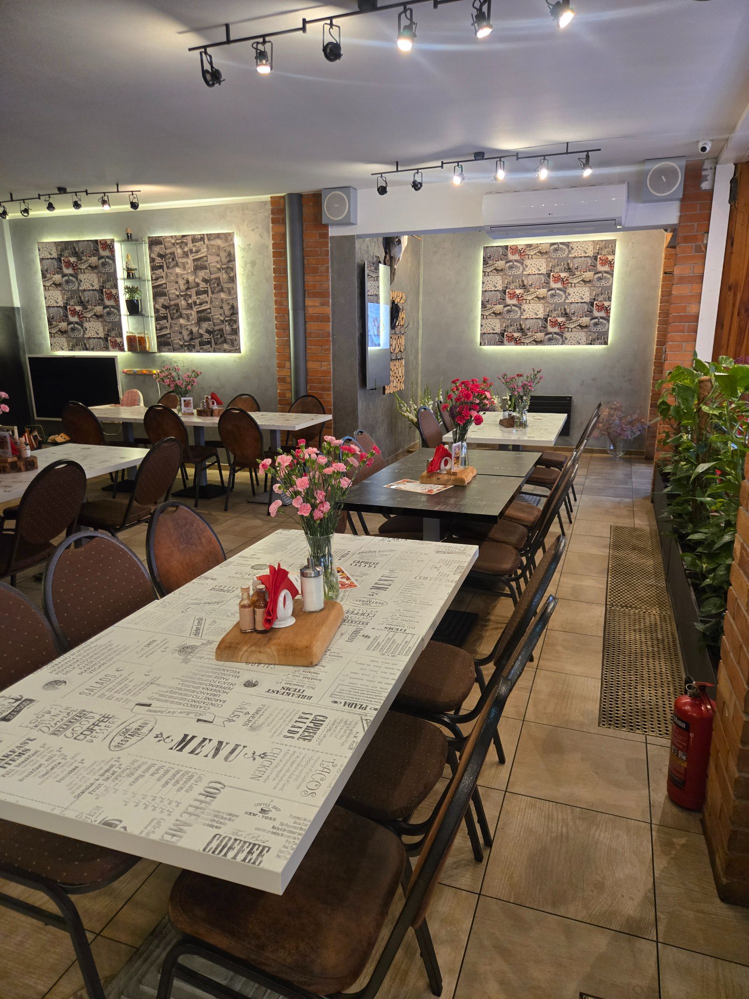 Wnętrze restauracji z ustawionymi stołami, krzesłami i ozdobnymi kwiatami na każdym stole.
