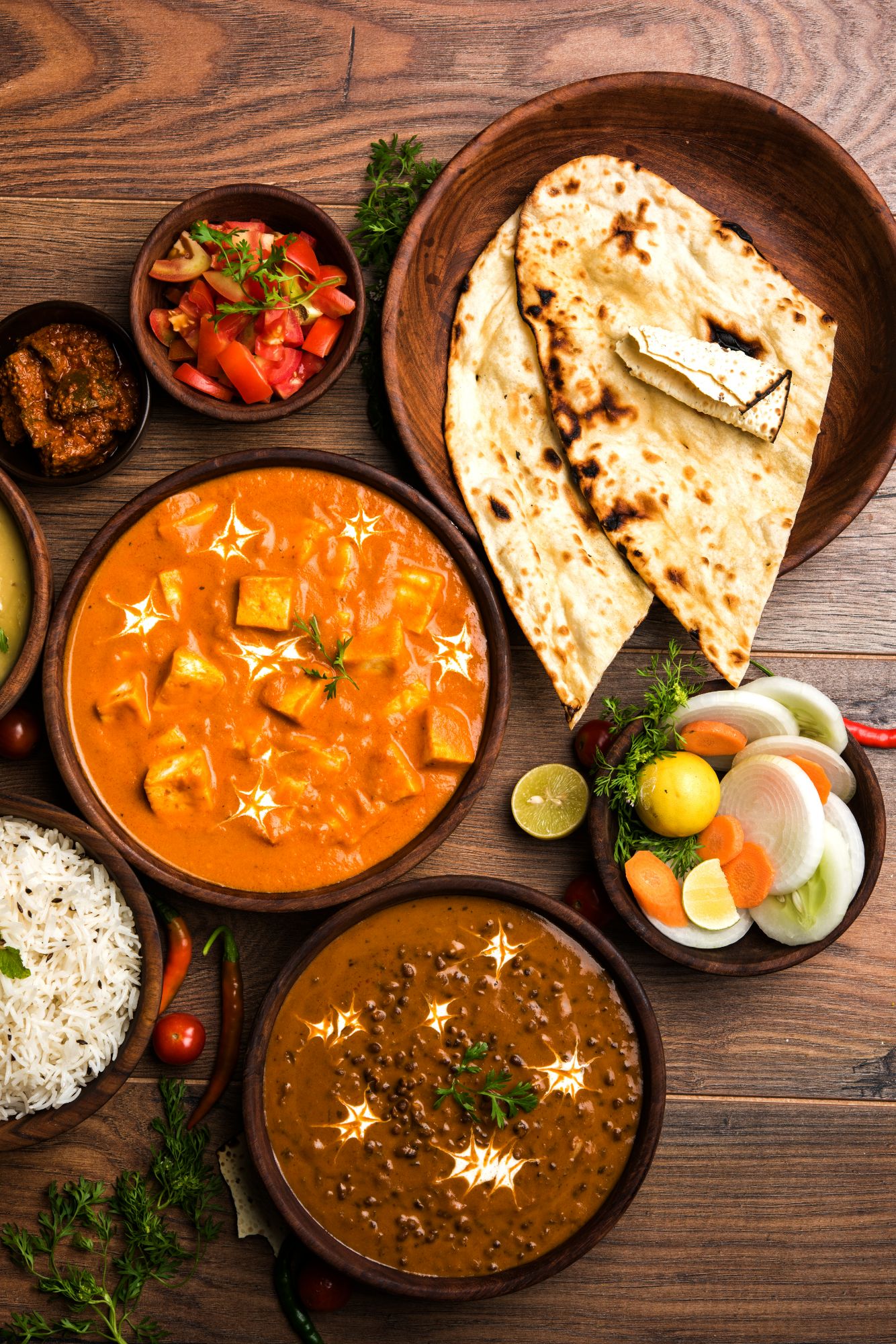 Aromatyczne indyjskie dania: curry, ryż, chleb naan oraz świeże warzywa w miseczkach.