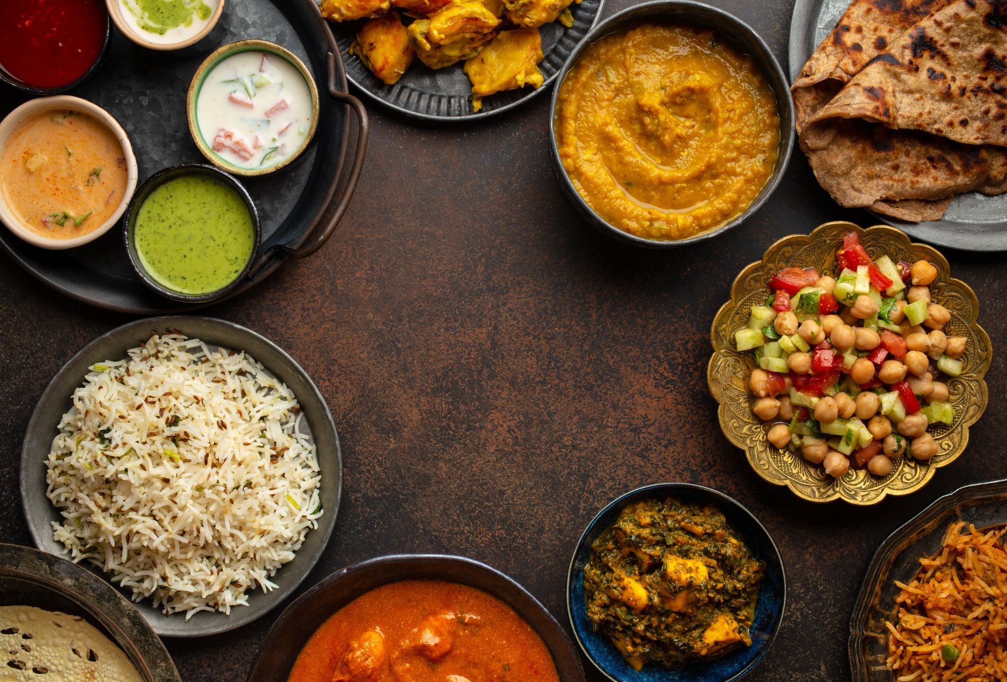 Różnorodne dania indyjskie na talerzach: curry, ryż, sałatki, naan oraz sosy w atmosferze rustykalnej.