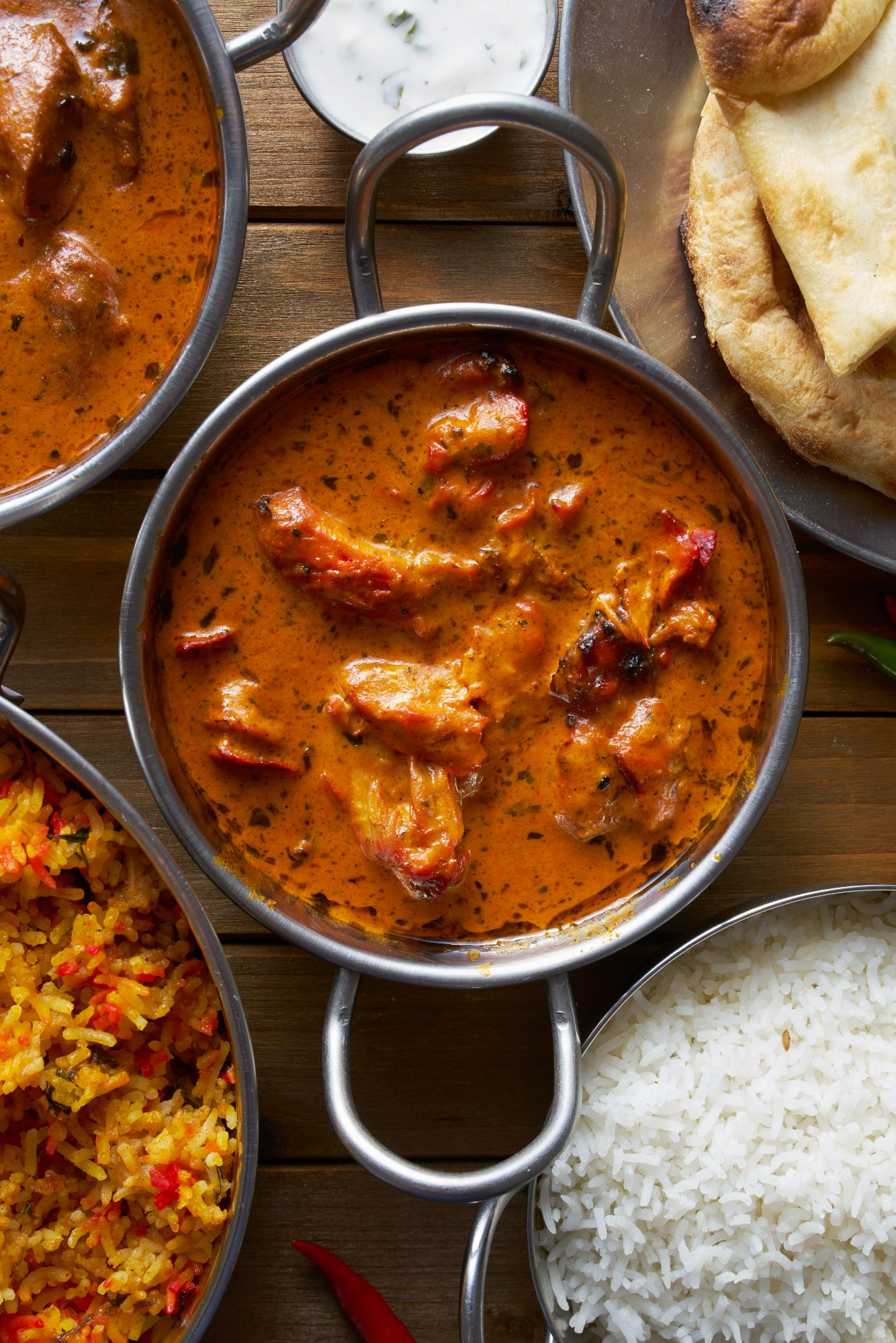 Miska curry z mielonym mięsem i pomidorami, obok ryż, biryani i chleb naan na drewnianym stole.
