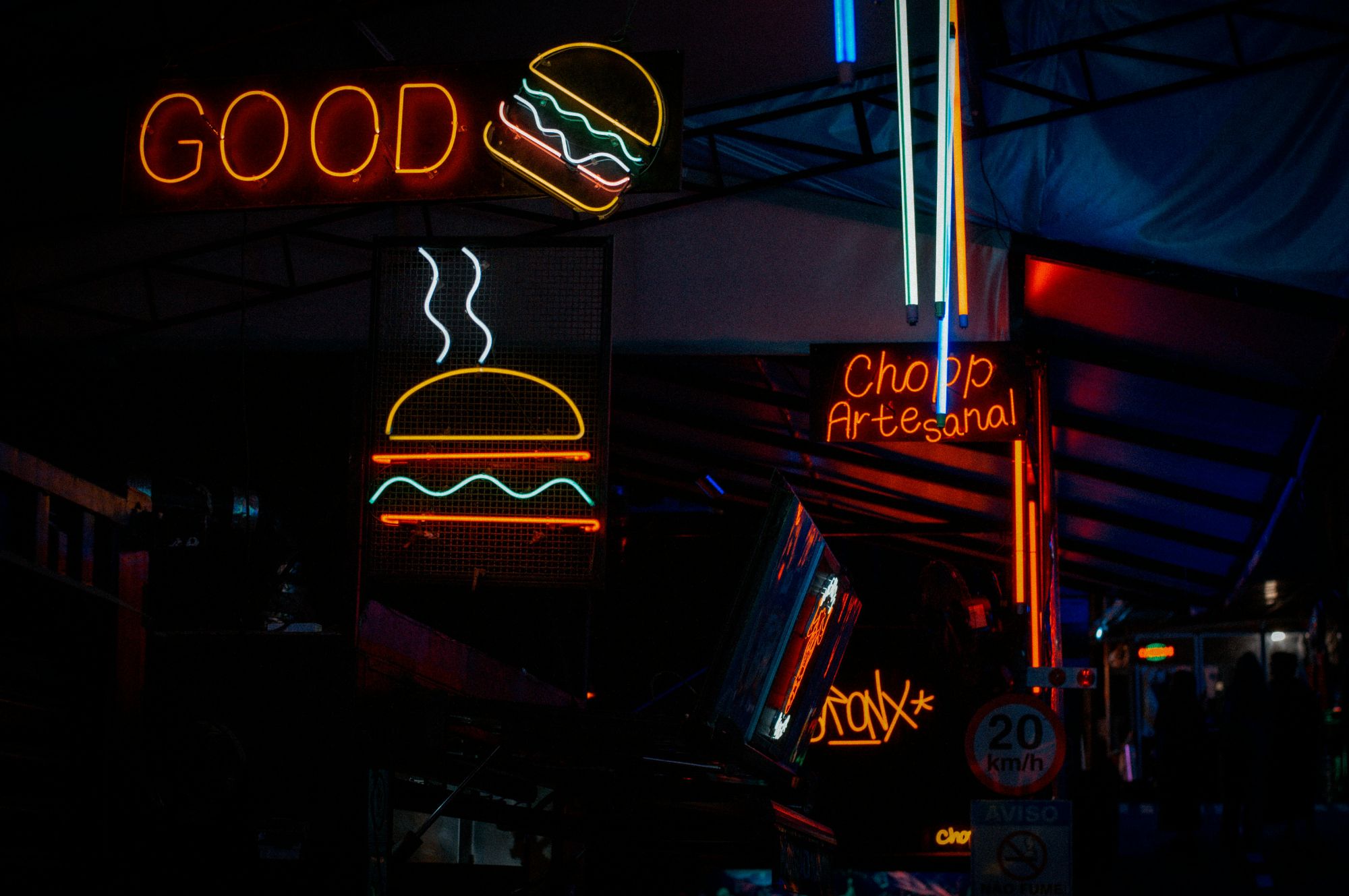 Neonowe znaki "GOOD" i "Chopp Artesanal" z hamburgerem w ciemnym otoczeniu.