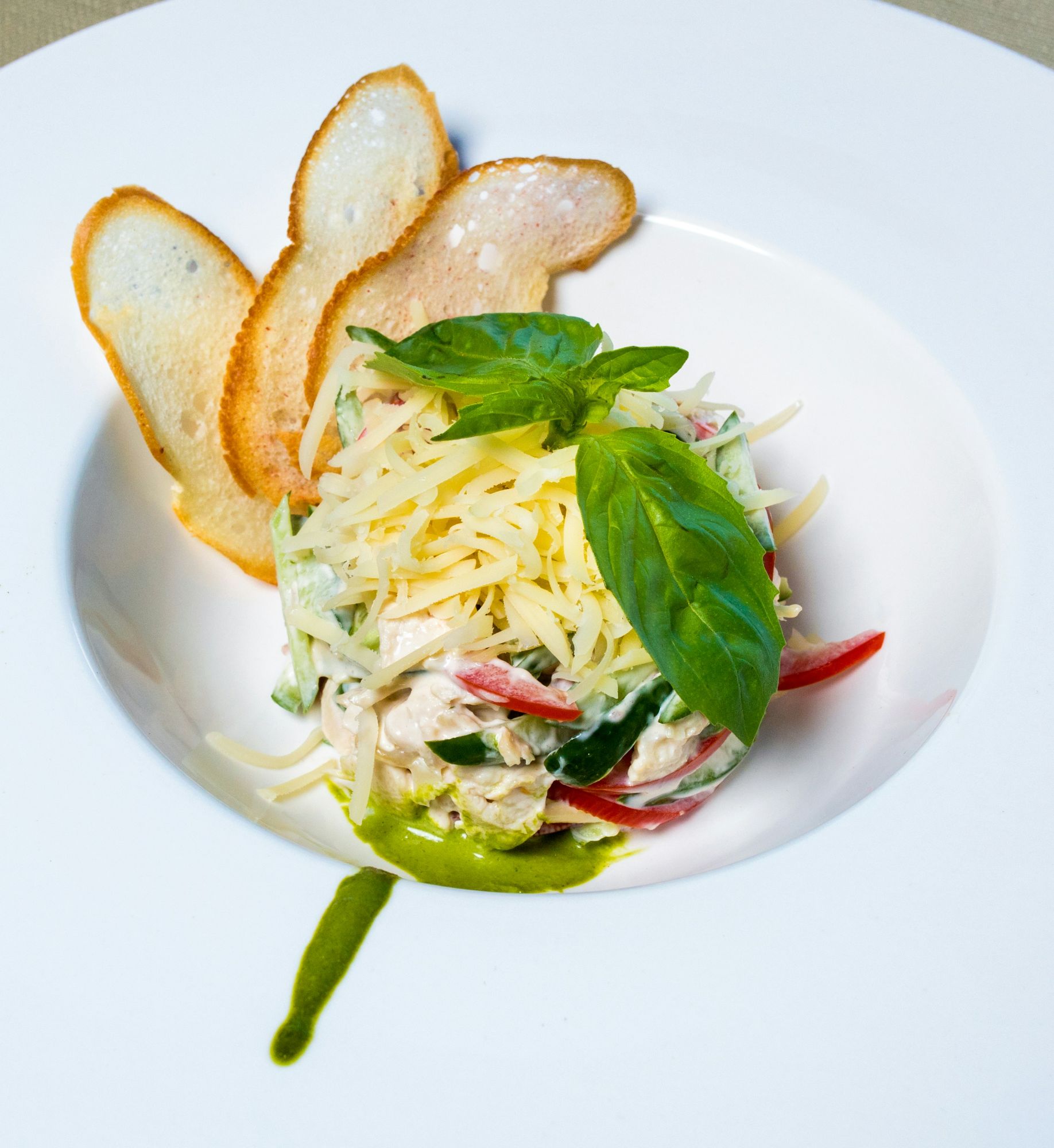 Salată de pui cu legume, brânză cheddar rasă și frunze de busuioc, servită cu felii de pâine crocantă.