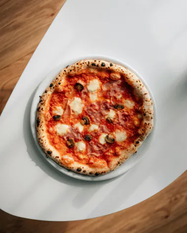 Pizza margherita cu crustă rumenită, asezată pe o farfurie albă, pe un suport de masă din lemn.