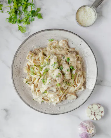 Paste fettuccine cu sos alb cremos, ciuperci și usturoi, presărate cu brânză și pătrunjel proaspăt.