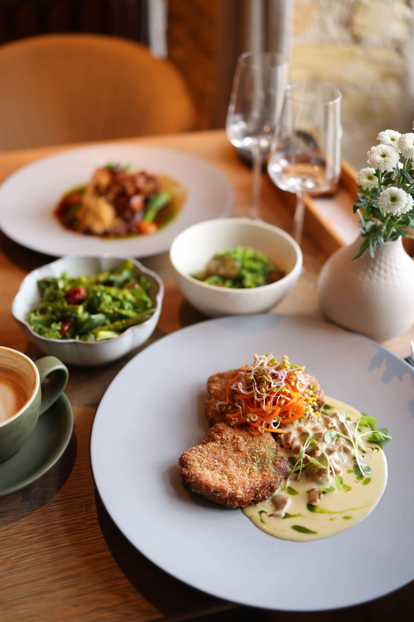 Plater z jedzeniem: kotlet, sałatka, zupa, filiżanka kawy i kieliszki, na tle estetycznego wnętrza.