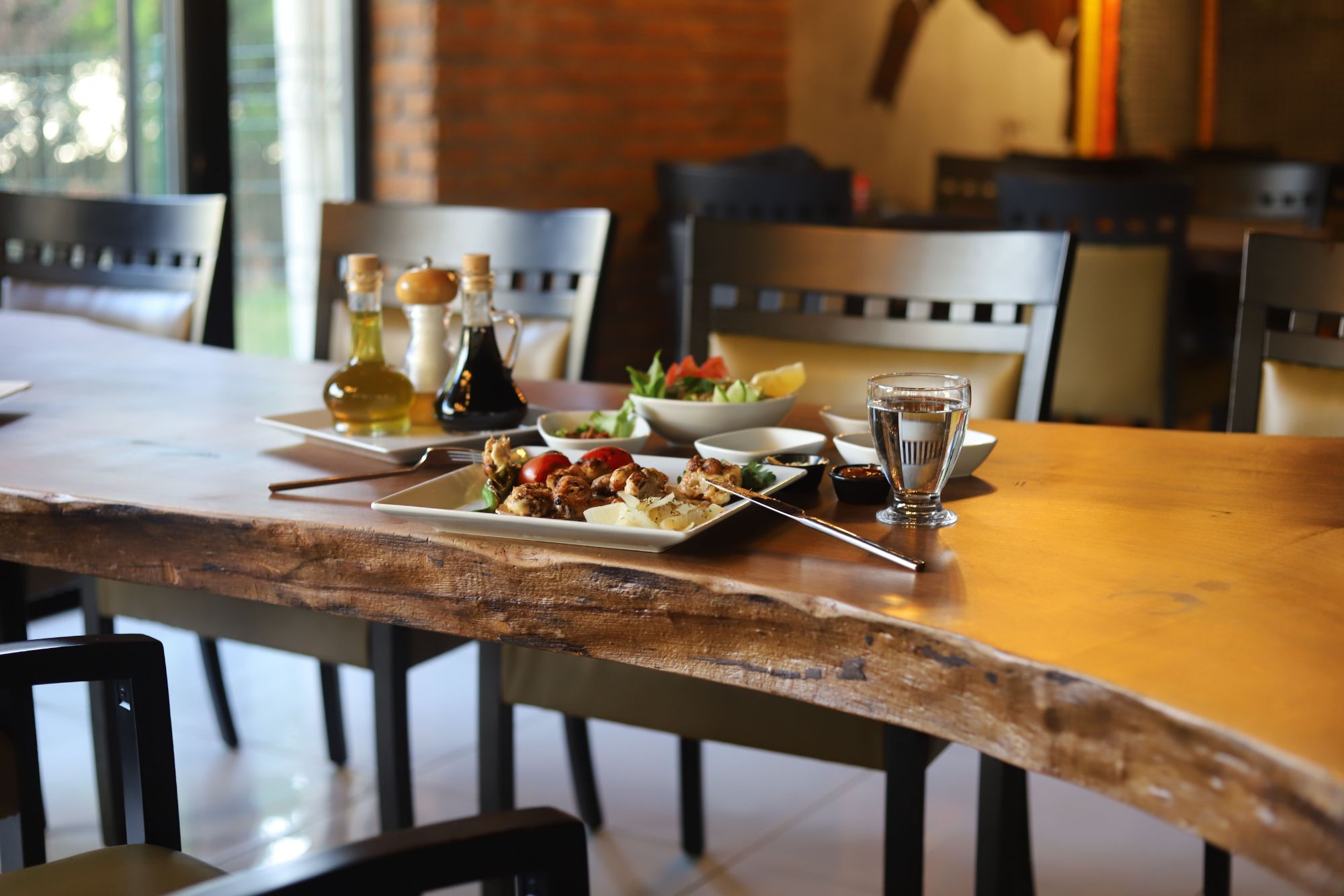 Stół w restauracji z potrawami, oliwą, przyprawami oraz sałatką w przyjemnym otoczeniu.