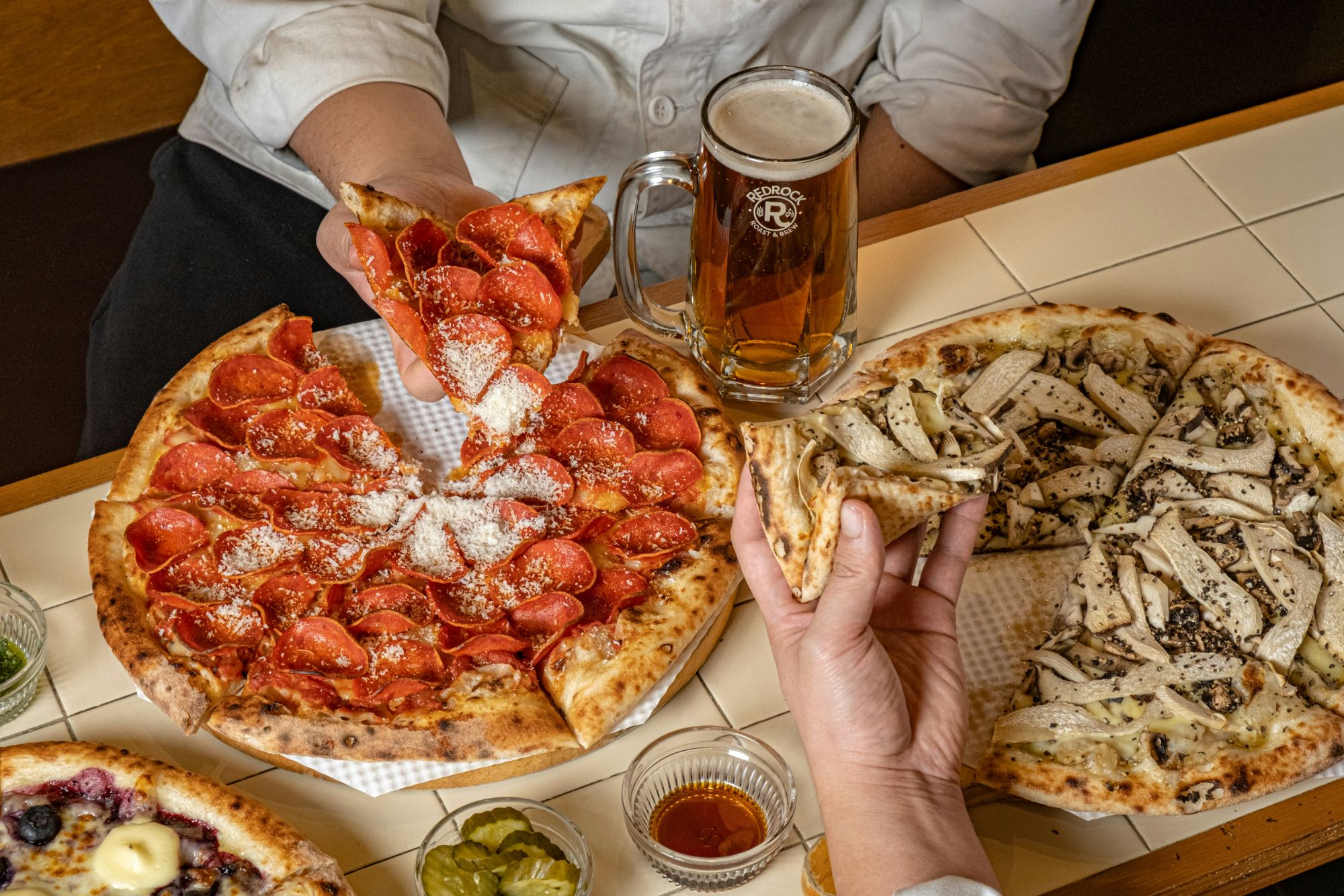 Pizza z pepperoni i serem, piwo w kuflu, różne rodzaje pizzy na stole.