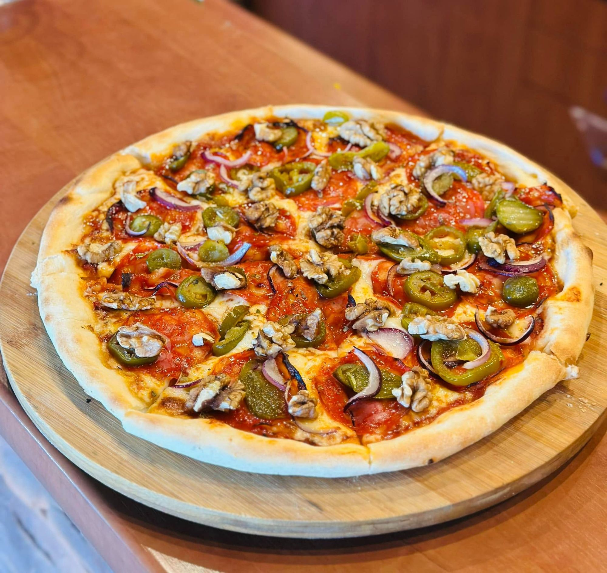Pizza z salami, jalapeño, orzechami i cebulą na drewnianej desce.
