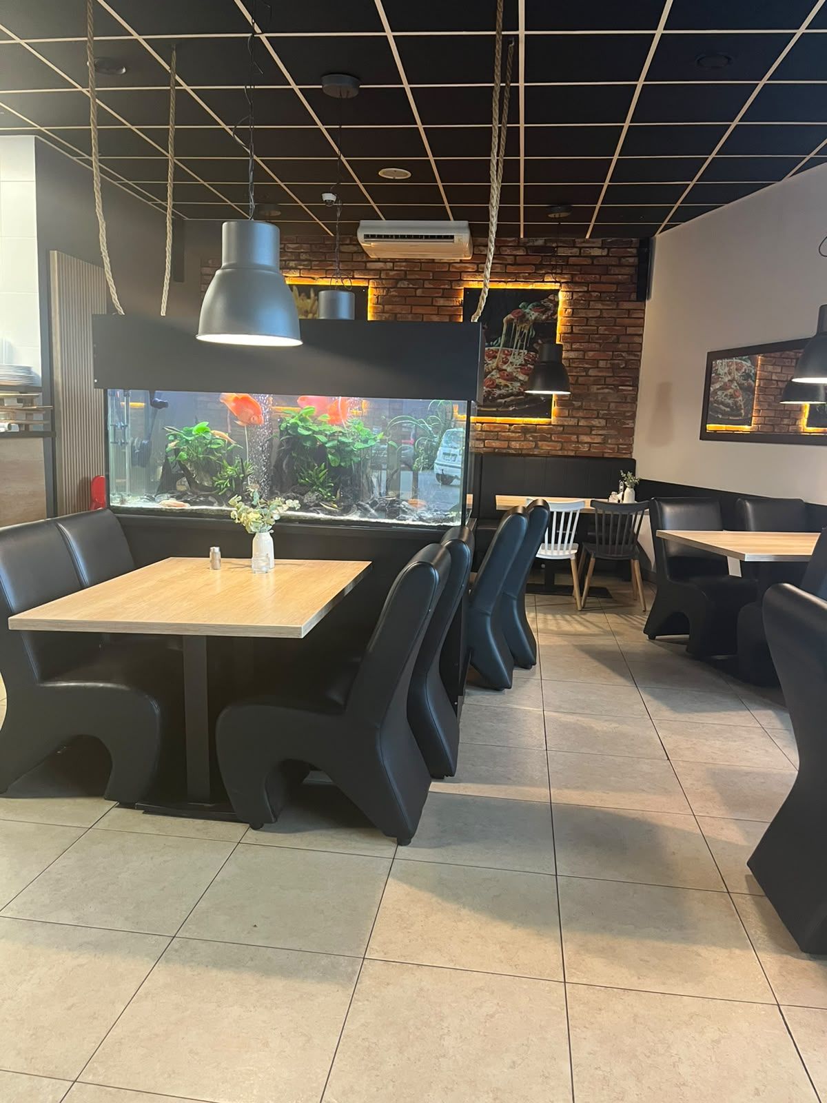Wnętrze nowoczesnej restauracji z akwarium i eleganckimi meblami, strefy do siedzenia oraz kamienną ścianą.