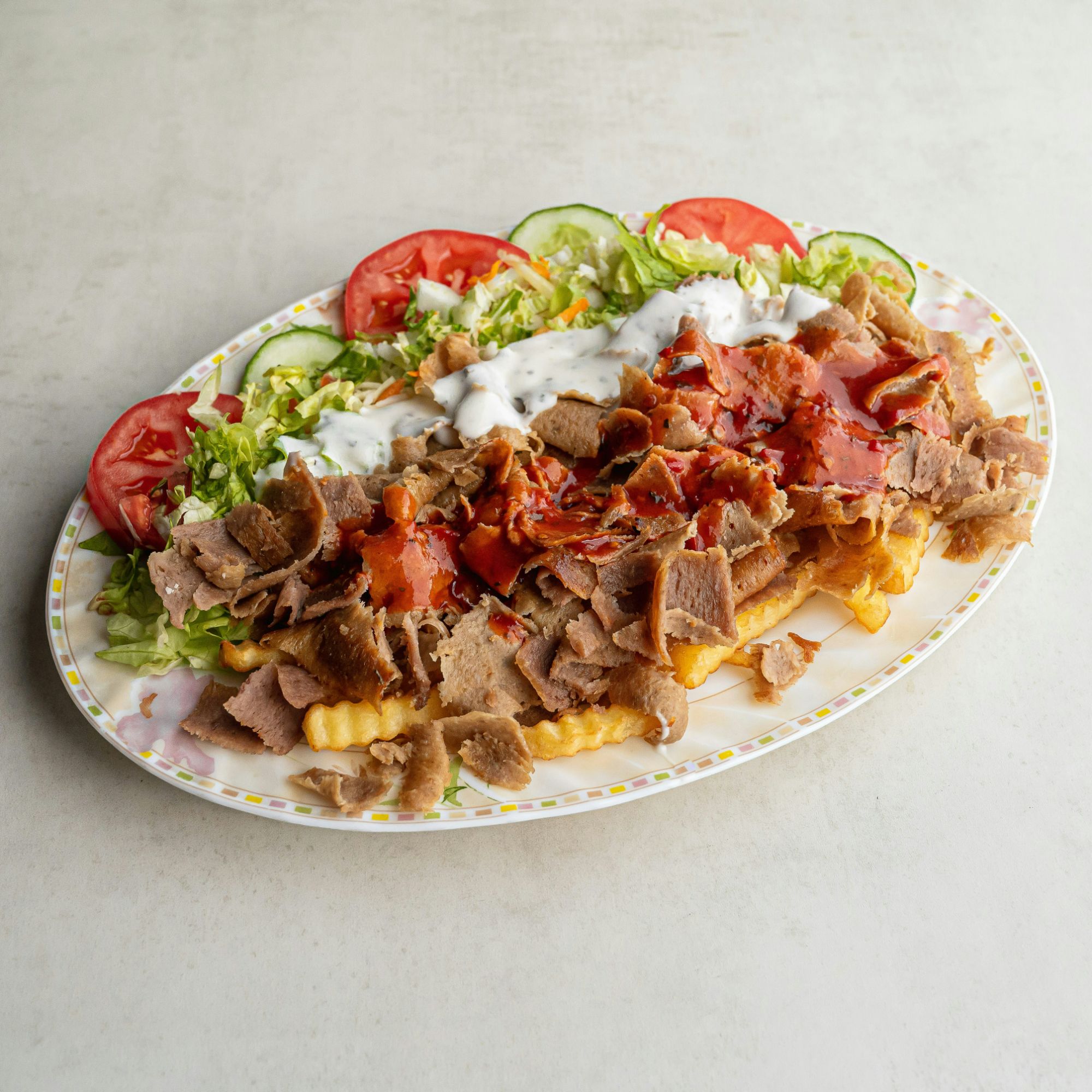 Talerz z frytkami, mięsem kebab, sałatą, pomidorami, ogórkiem i sosem.