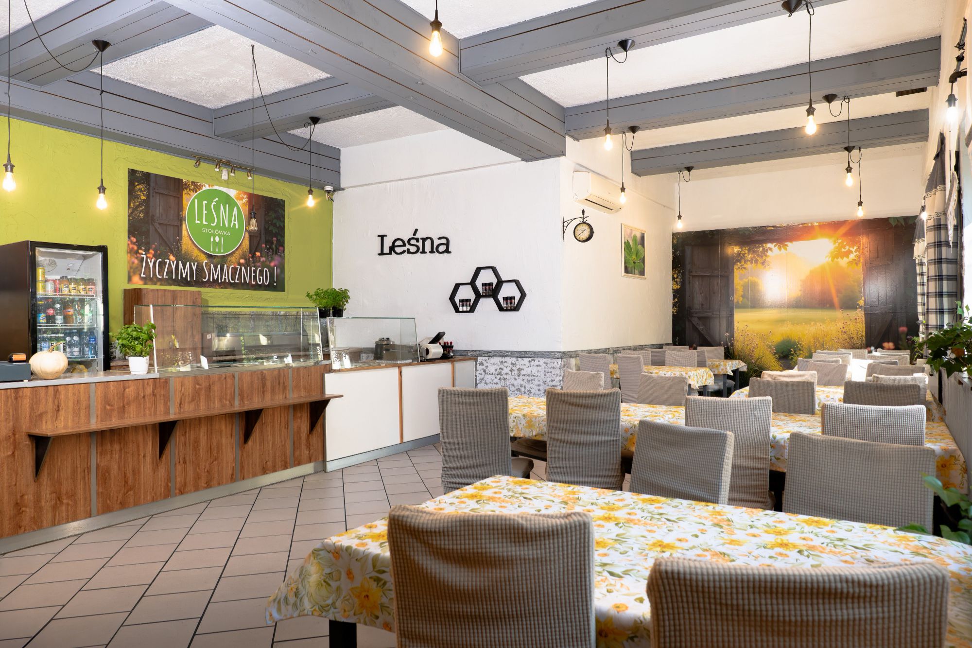Nowoczesna restauracja z jasnymi wnętrzami, stołami z kwiecistymi obrusami i przytulnymi dekoracjami.
