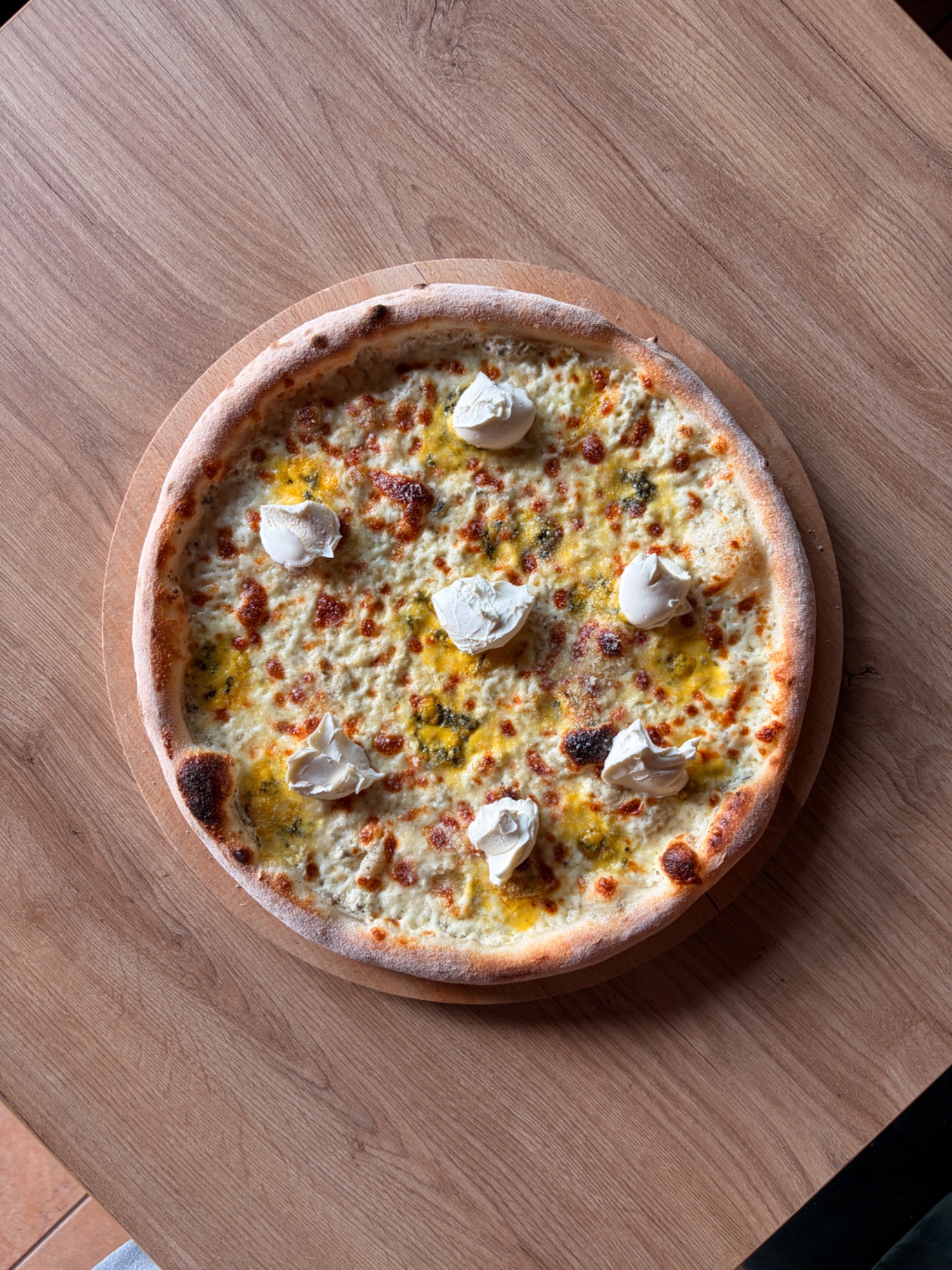 Pizza z serem i kawałkami kremowego nadzienia na drewnianej desce.