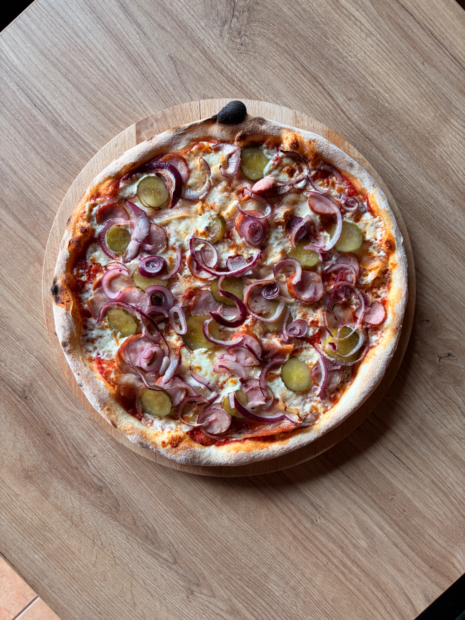 Pizza z sosem pomidorowym, serem, cebulą i ogórkami kiszonymi na drewnianej desce.