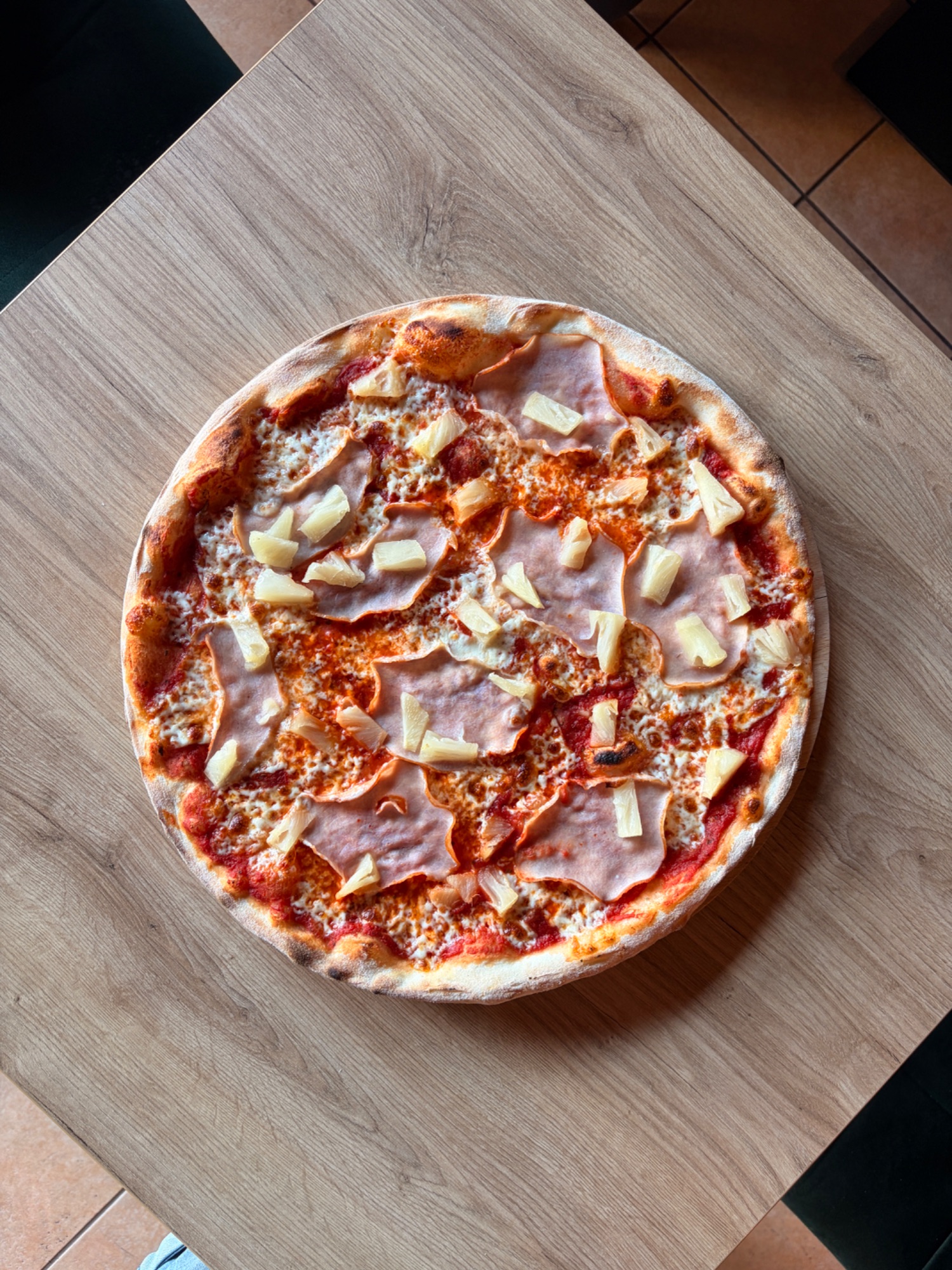 Pizza z szynką i ananasem na drewnianym stole.